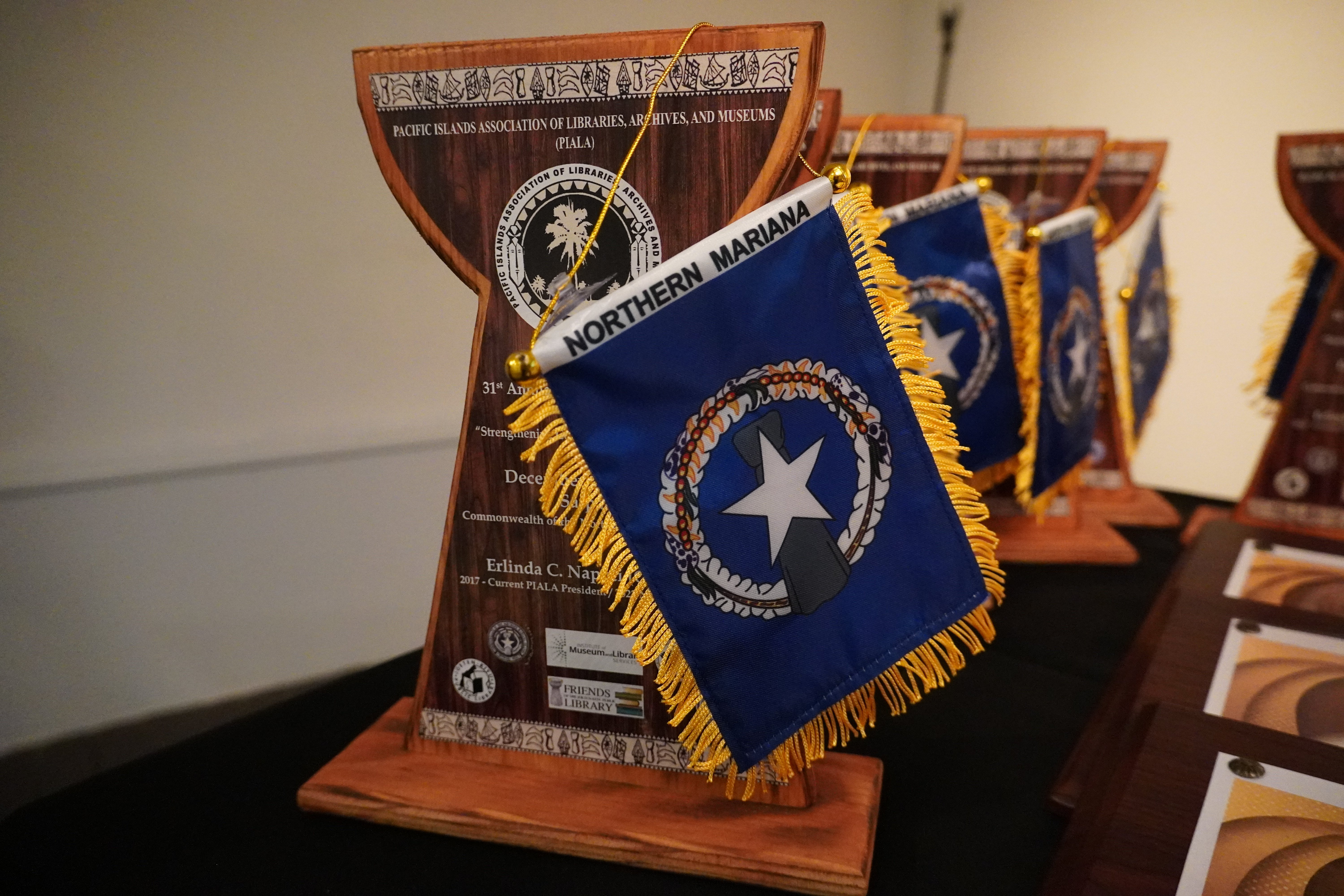 Wooden latte stone-shaped plaques with NMI flags sit atop a table, ready to be presented to each delegation. 