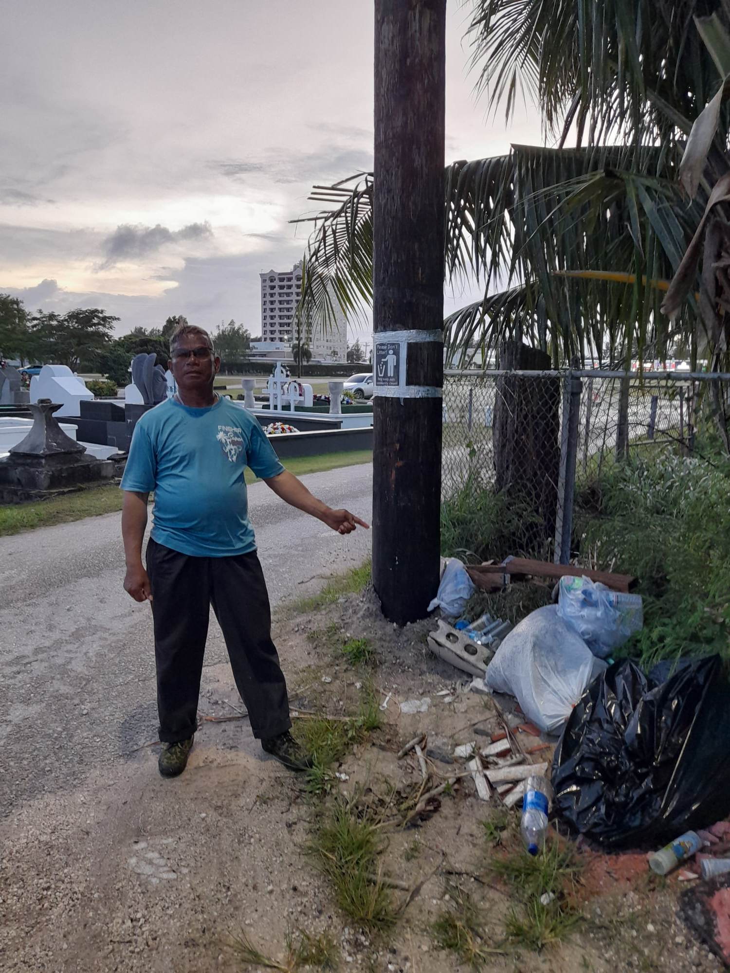 Community volunteer Max Aguon points to the trash dumped at the Chalan Kanoa cemetery near a sign that says “Please Don’t Litter” on Dec. 22, 2022.