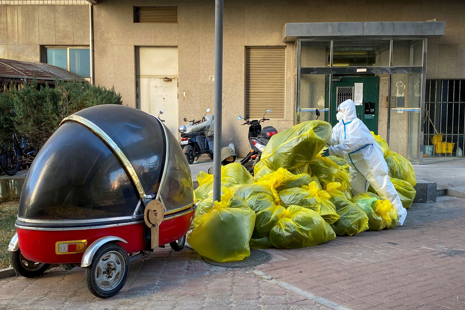 A pandemic prevention worker in a protective suit piles up bags of medical waste outside a building where residents isolate at home as coronavirus disease outbreaks continue in Beijing, Dec. 5, 2022.