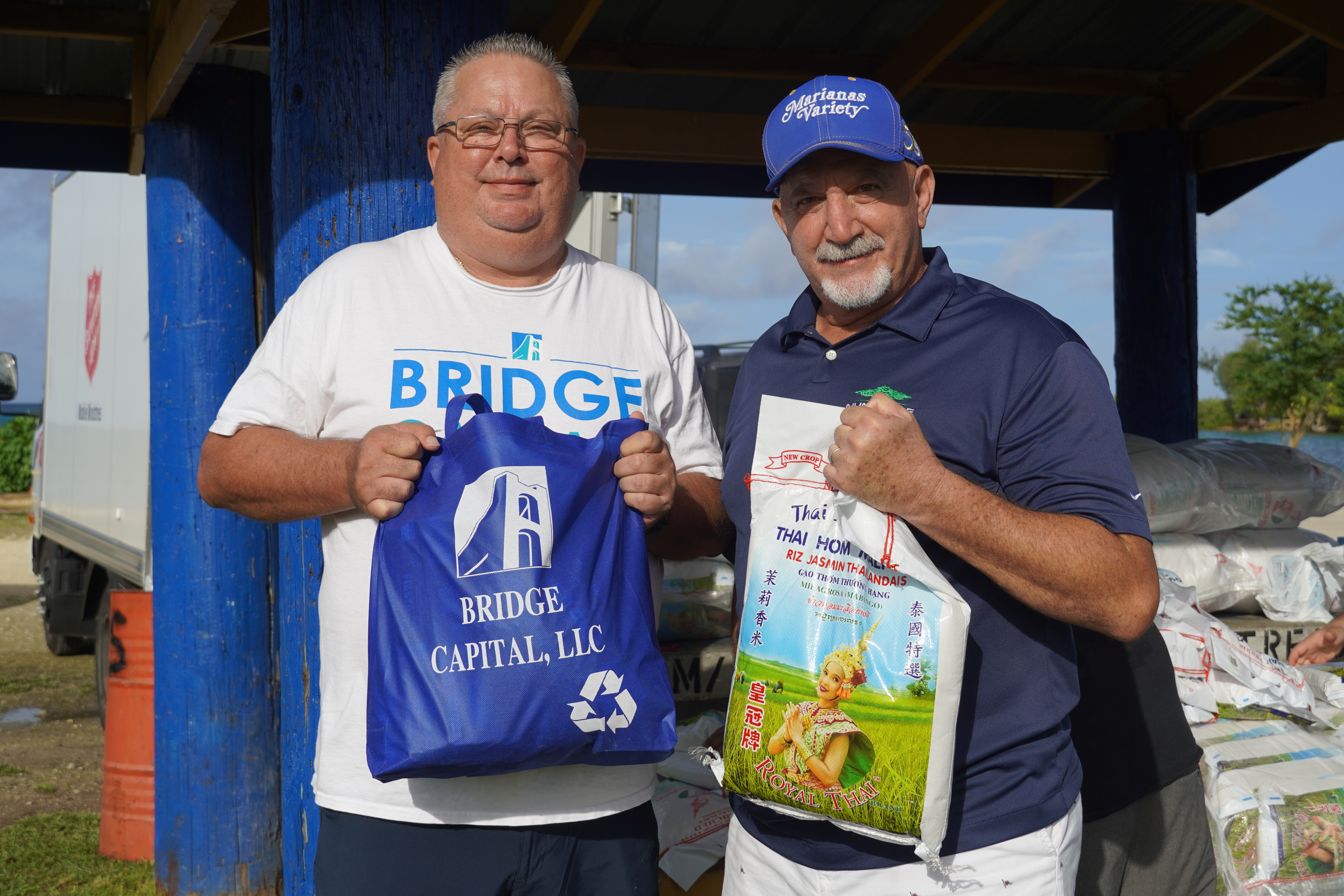 Bridge Capital LLC general manager Bart Johnson, right, and a colleague pose for a photo with a bag of rice and a reusable bag filled with food.