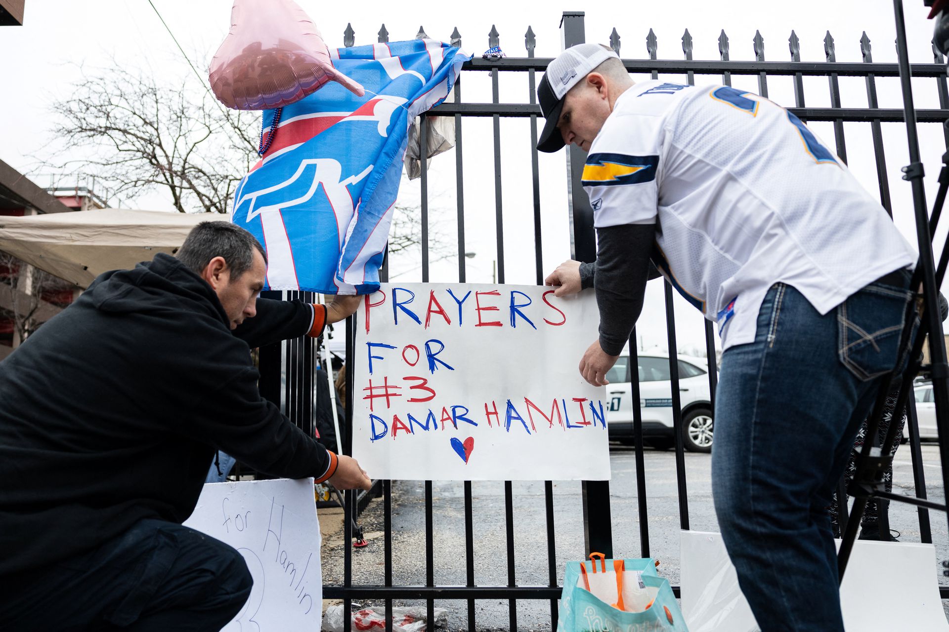 Football fans tape a sign to a fence during a vigil outside the University of Cincinnati Medical Center where Buffalo Bills safety Damar Hamlin lies in critical condition, after suffering a cardiac arrest during the Jan. 2 National Football League  game against the Cincinnati Bengals, in Cincinnati, Ohio, Jan. 3, 2023.
