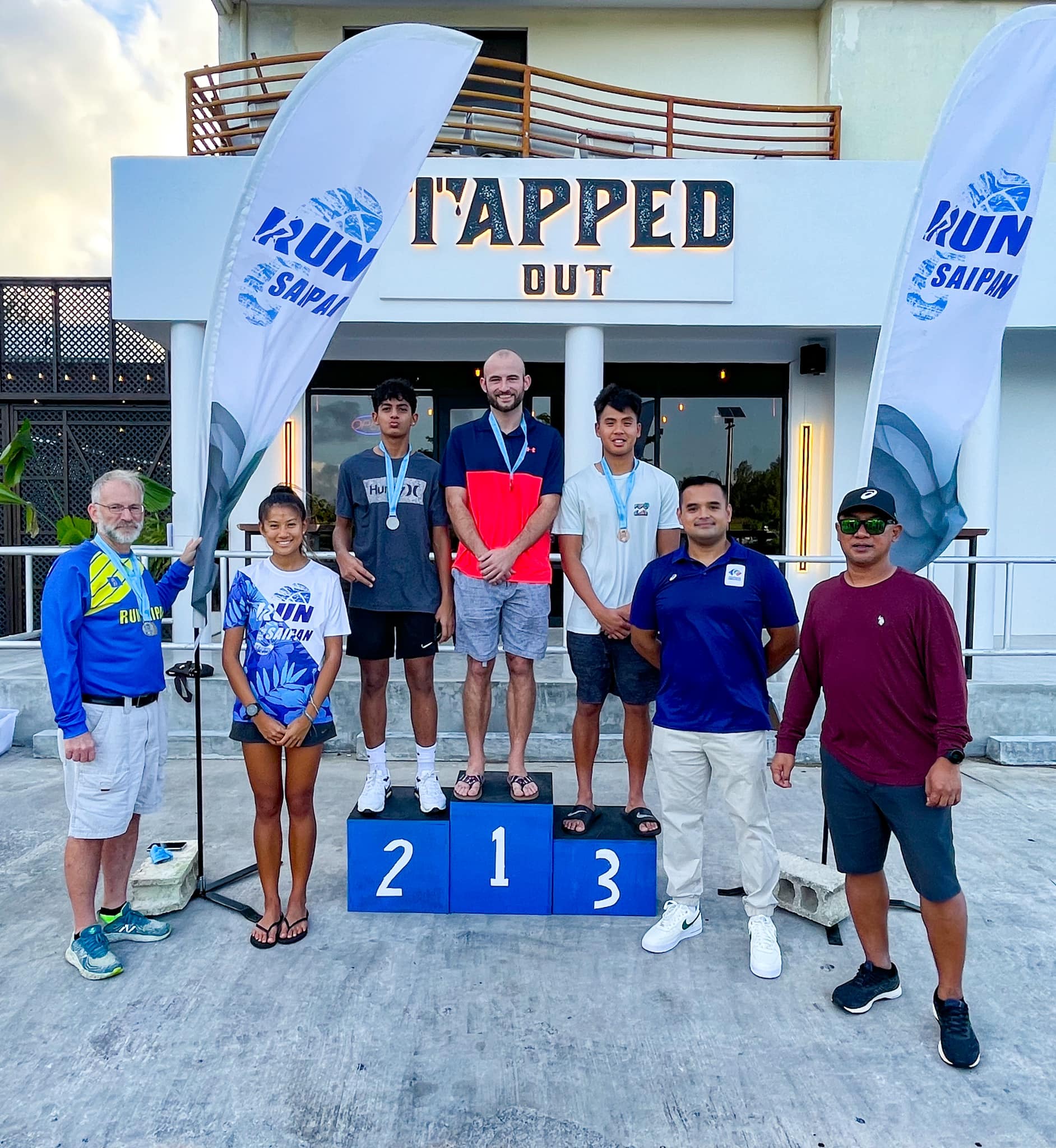 Keither Ketola, Dev Bachani and Heimanarii Lai pose on the podium with their medals during the Run From '22 awards ceremony on Saturday. Also in photo: Tania Tan and Run Saipan officers.