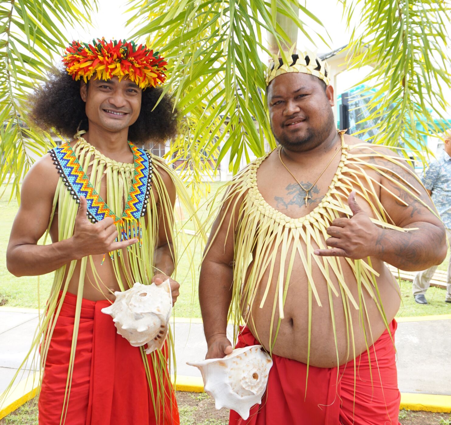Two Refaluwasch men pose for a photo, each holding a sawi, or conch shell.