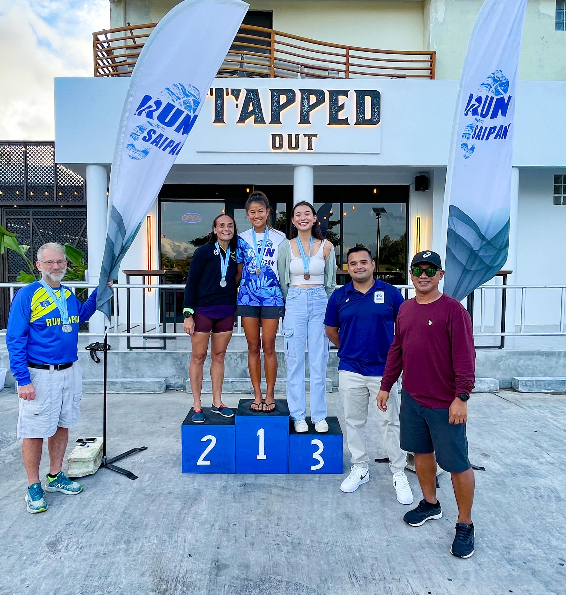 Tania Tan, Sharon Hawley and Tiana Cabrera pose on the podium with their medals during the Run From '22 awards ceremony on Saturday. Also in photo: Run Saipan officers.