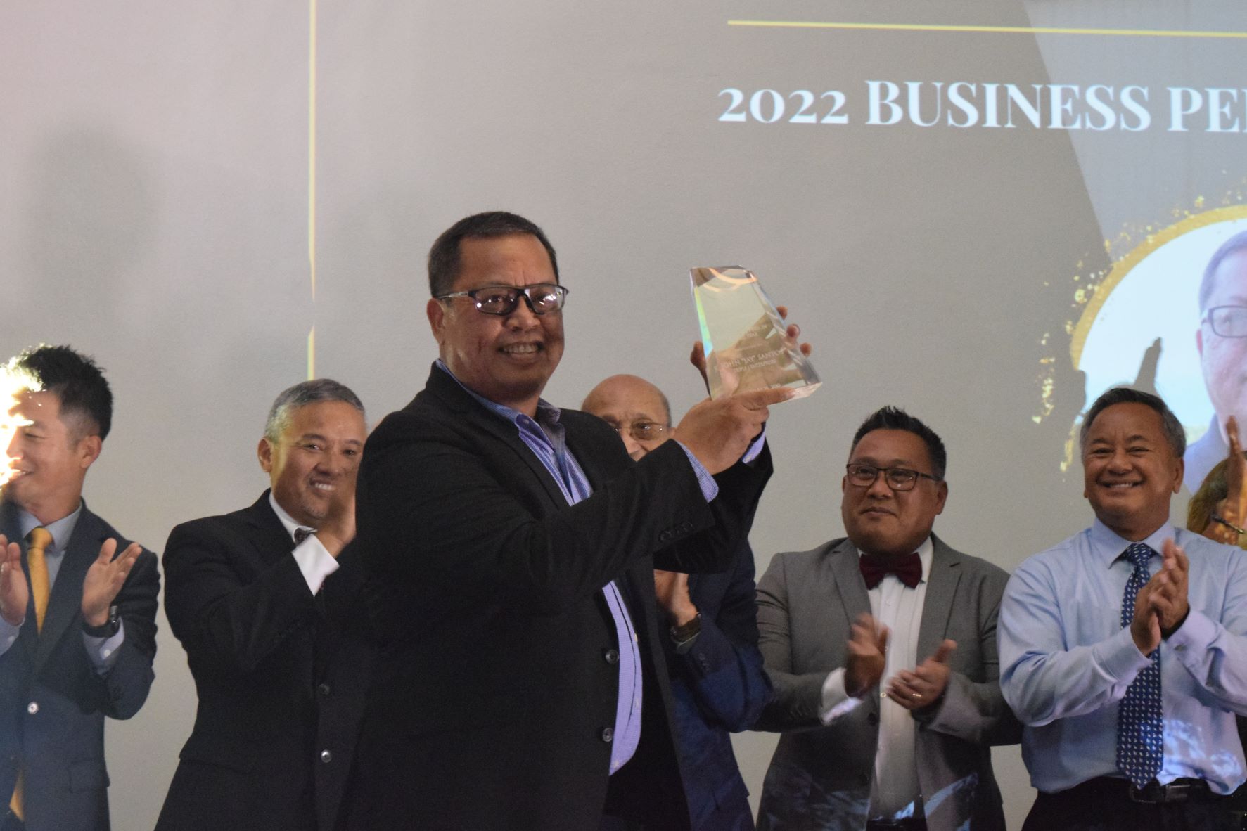 Triple J Five Star Wholesale Foods and Triple J Payless SuperFresh &Truckload Store General Manager John Jay Santos holds his Saipan Chamber of Commerce 2022 Business Person of the Year Award as past awardees — E-Land's Brian Shin, Tan Holdings' Alex Sablan, David M. Sablan Sr., and Ivan Quichocho, and Triple J's Mike Sablan — applaud during the chamber's annual gala at the Crowne Plaza Resort on Saturday.