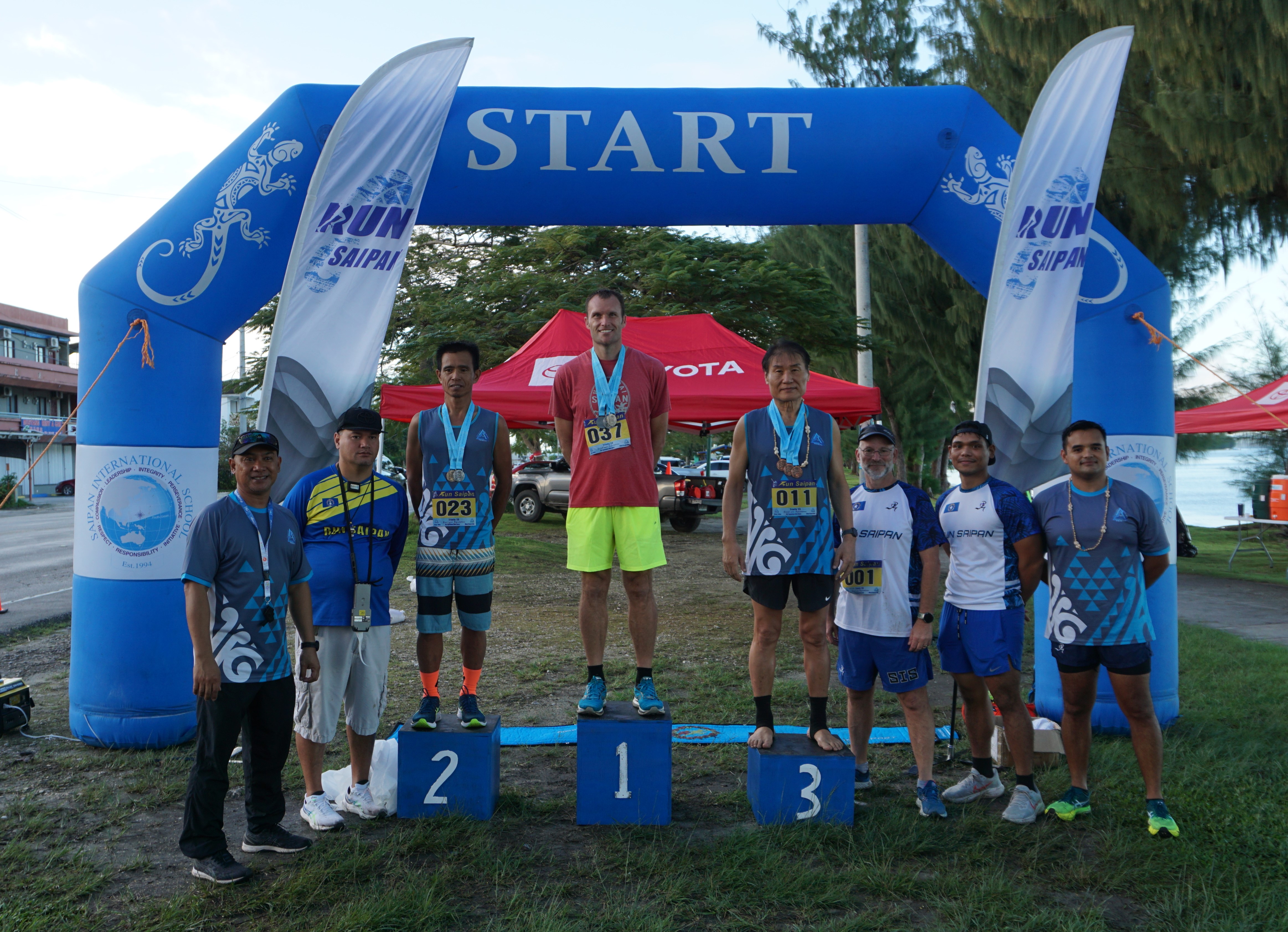 The top three men runners — Chad Taflinger, Joel Buco and Chong Nam Lee — pose with Run Saipan officials during the awards ceremony Monday on Beach Road in Oleai.