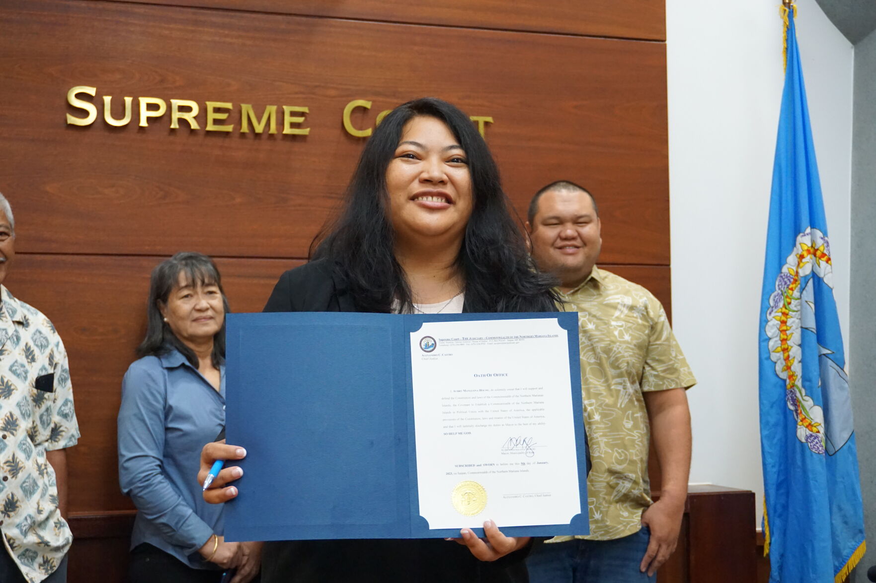 Rota Mayor Aubry M. Hocog smiles as she holds her signed oath of office with her family in the background.