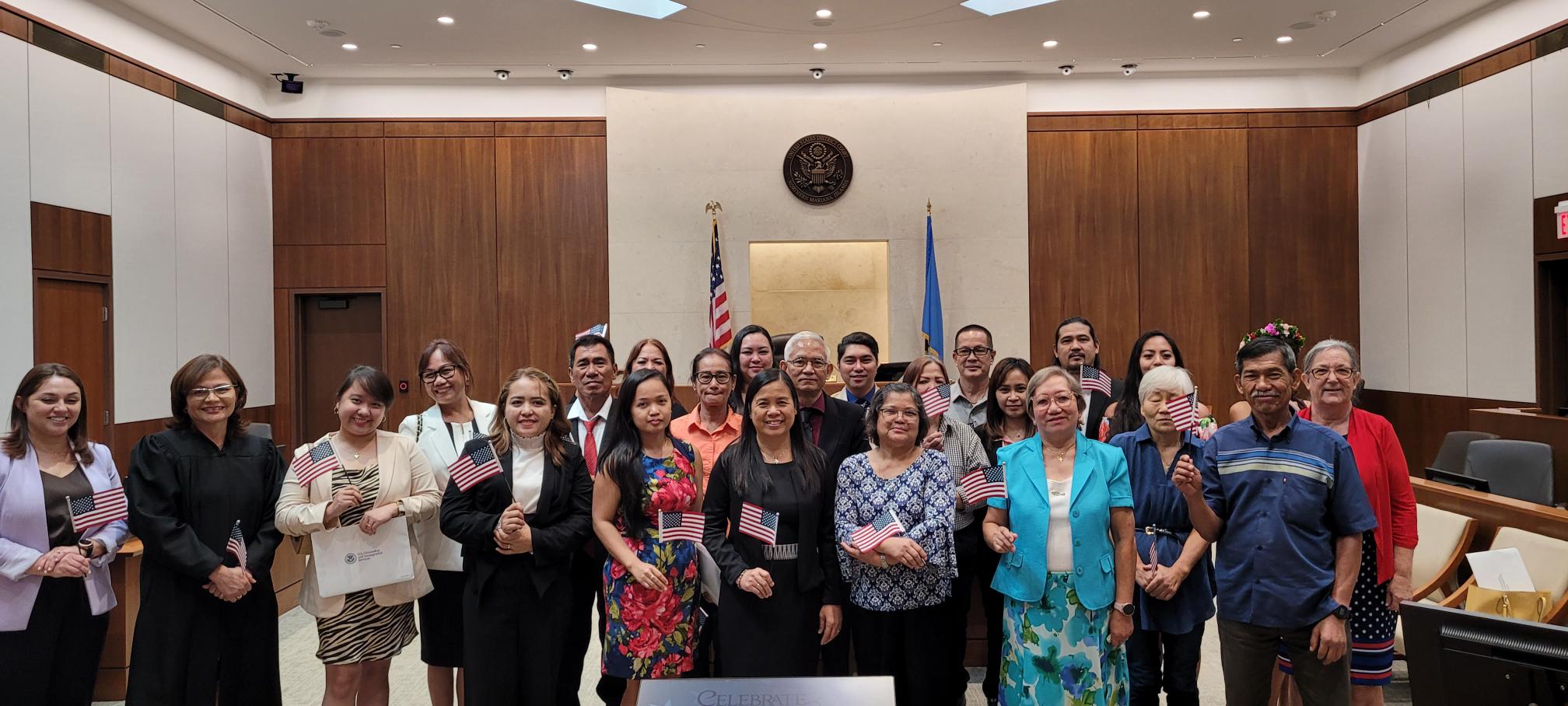 The 21 new U.S. citizens with District Court for the NMI Chief Judge Ramona Manglona, attorney Charity Hodson, and Patricia Phelan, U.S. Citizenship and Immigration Services officer.