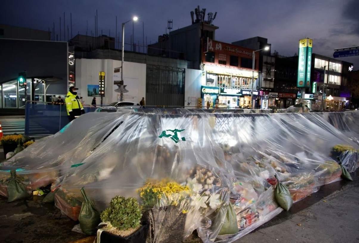 A police officer stands guard near floral tributes at the scene of a crowd crush that happened during Halloween festivities in Seoul, South Korea, Nov. 29, 2022.