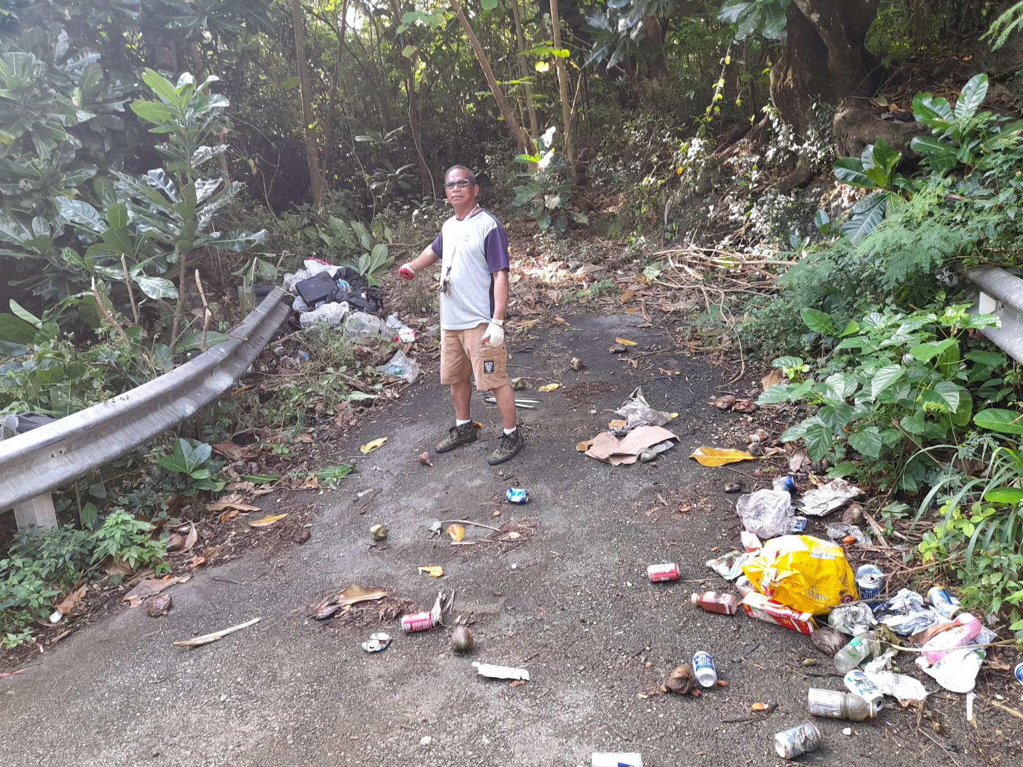 Community volunteer Max Aguon points to the household trash dumped on the road headed to Laulau Bay.