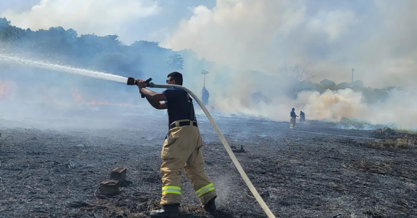 A firefighter aims a hose at the grassfire in Marpi on Monday.