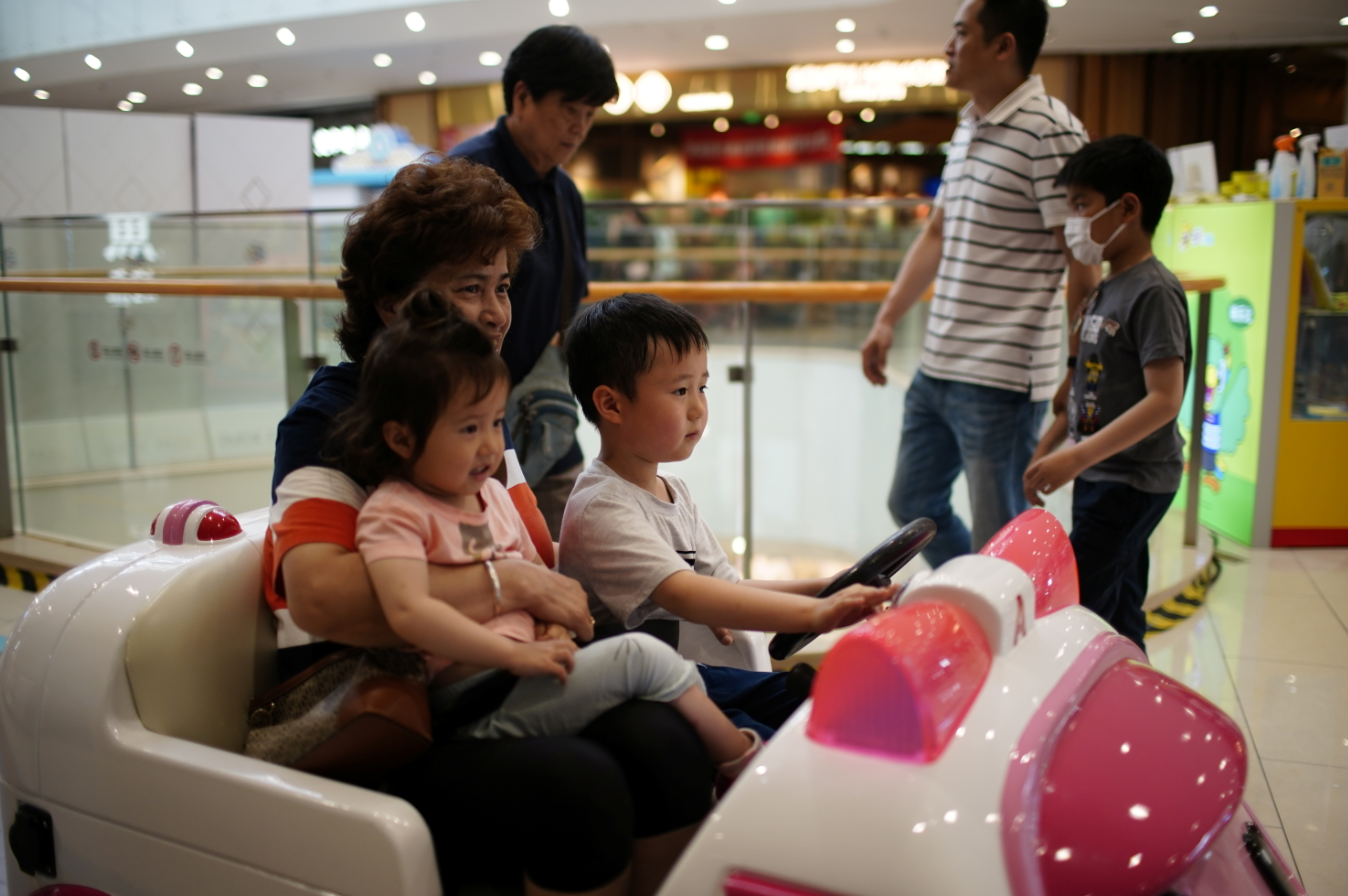 A woman holds a girl as a boy drives a toy car at a shopping mall in Shanghai, China, June 1, 2021.