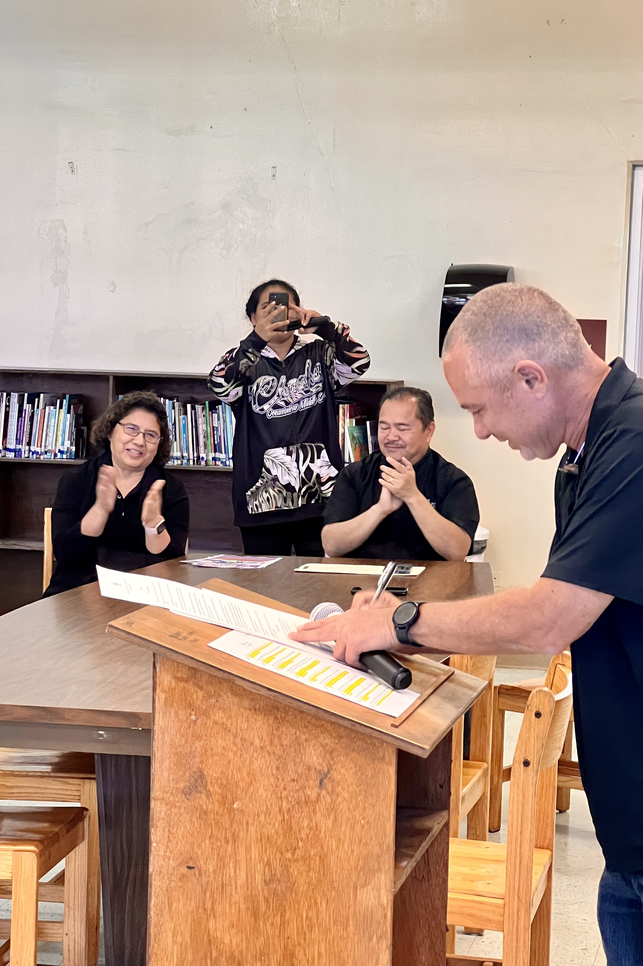 Board of Education Secretary/Treasury Gregory Pat Borja signs the  School Library Month proclamation while Commissioner of Education Dr. Alfred B. Ada and Senior Director Jackie Quitugua applaud.