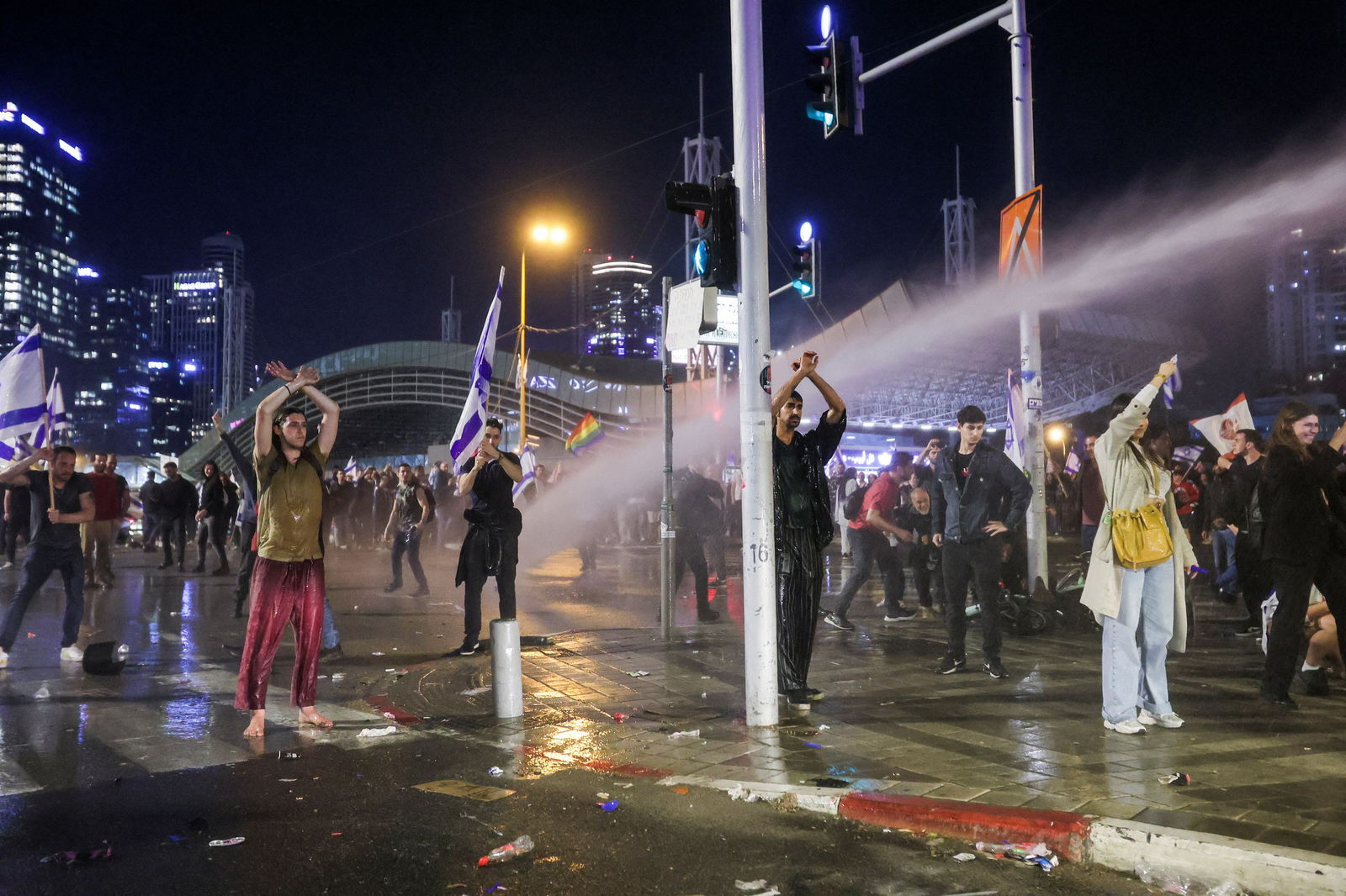 Israeli protesters stand with their arms up as a water cannon is used to disperse the people attending a demonstration against Israeli Prime Minister Benjamin Netanyahu and his nationalist coalition government's plan for judicial overhaul, in Tel Aviv, Israel, March 27, 2023.