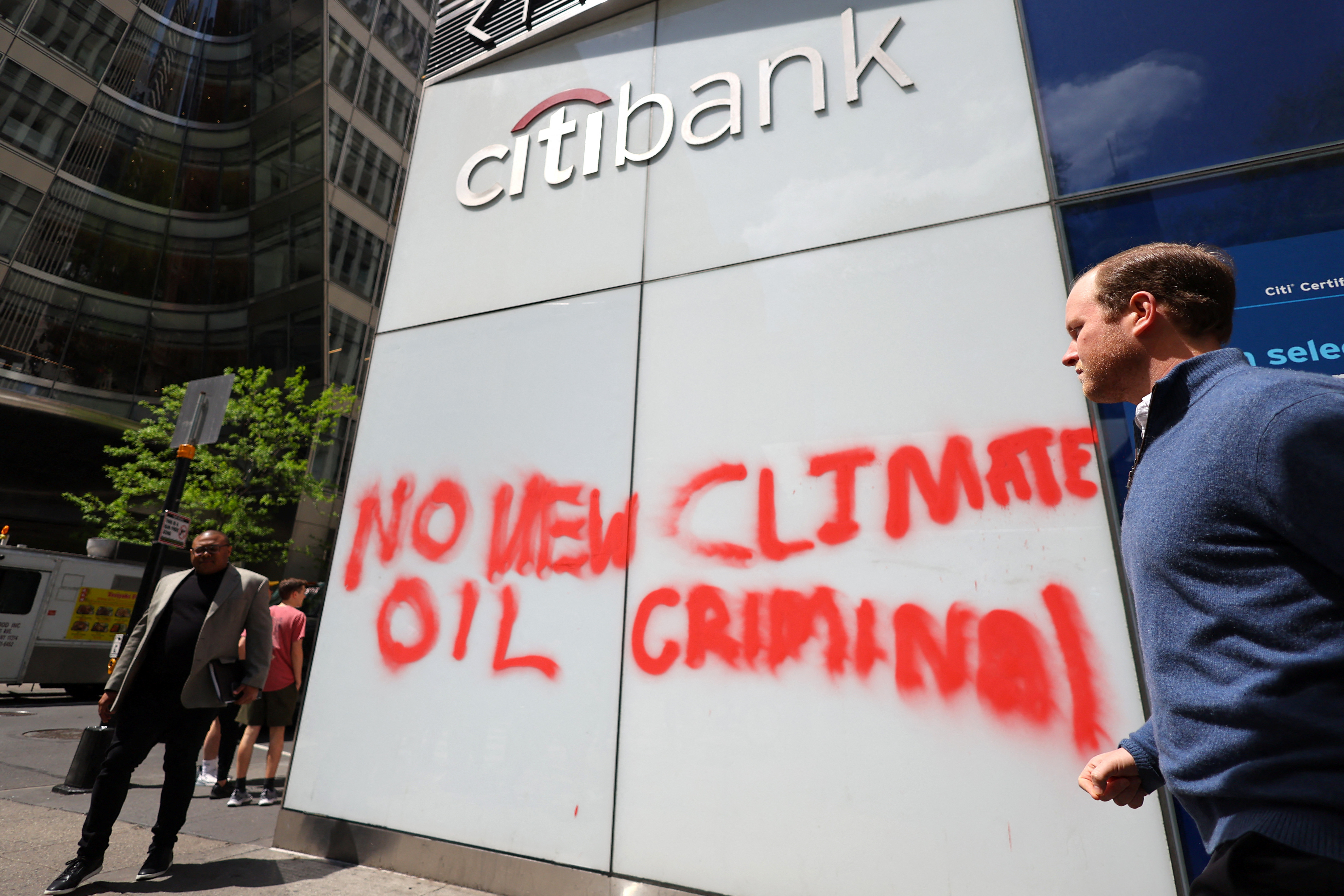 People walk past a spray-painted message left by climate protestors on the outside of a Citibank branch in Midtown Manhattan in New York City, New York, U.S., April 24, 2023. REUTERS/Mike Segar