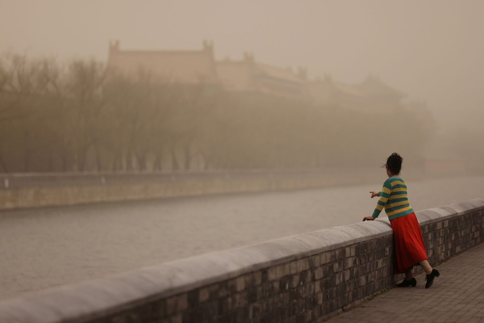 FILE PHOTO: A woman poses for pictures near the Forbidden City, as the city is shrouded in smog amid a sandstorm, in Beijing, China March 10, 2023. REUTERS/Tingshu Wang/File Photo