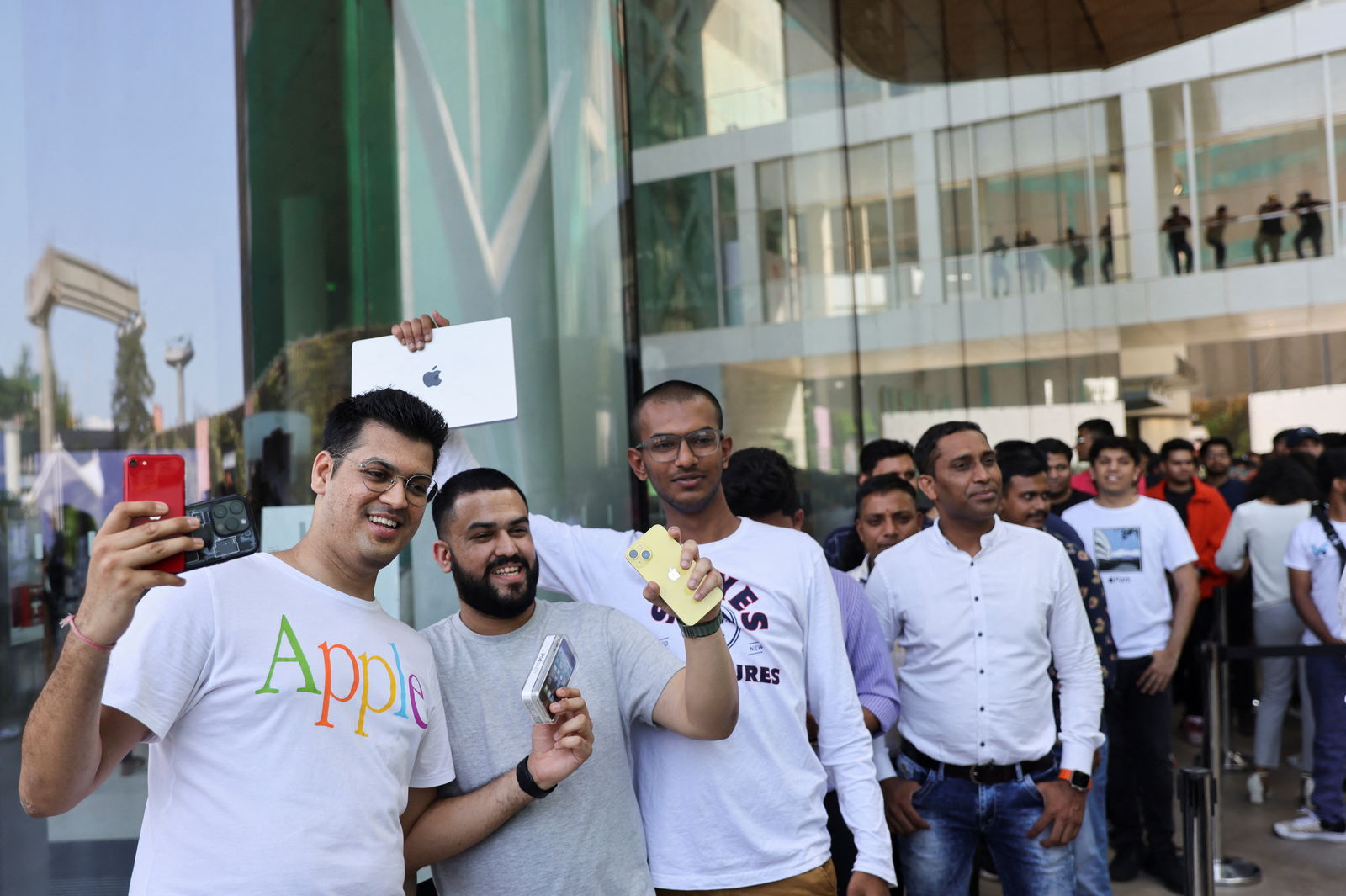 People pose with Apple products while waiting in a queue outside India's first Apple retail store, on the day of its opening in Mumbai, India, April 18, 2023. REUTERS/Francis Mascarenhas