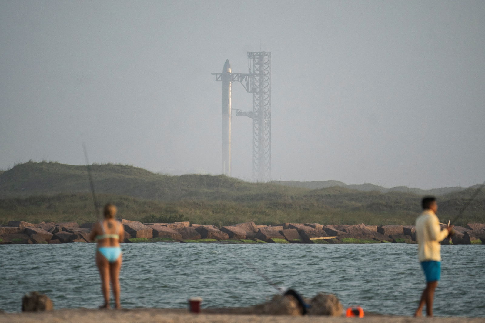 People fish at the beach park as the SpaceX Starship is seen on its Boca Chica launchpad following a postponement in its launch date due to a frozen valve near Brownsville, Texas, U.S., April 19, 2023. REUTERS/Go Nakamura