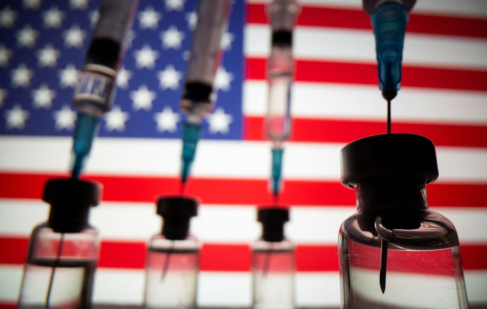 Vials and syringes are seen in front of displayed U.S. flag in this illustration photo taken March 16, 2021. REUTERS/Dado Ruvic/Illustration