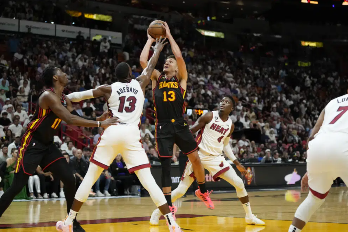 Atlanta Hawks guard Bogdan Bogdanovic (13) shoots from between Miami Heat center Bam Adebayo (13) and guard Victor Oladipo (4) during the first half of an NBA basketball play-in tournament game Tuesday, April 11, 2023, in Miami.