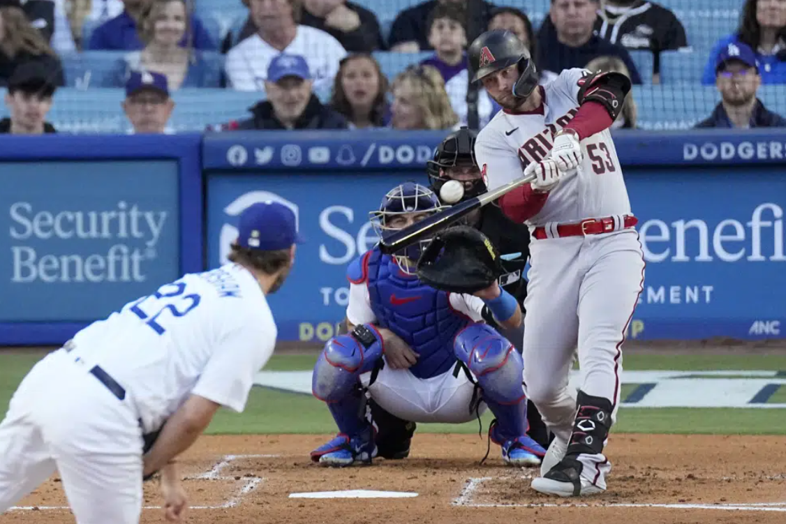 Arizona Diamondbacks' Christian Walker, right, hits a solo home run as Los Angeles Dodgers starting pitcher Clayton Kershaw, left, watches along with catcher Austin Barnes, second from left, and home plate umpire John Tumpane during the second inning of a baseball game Saturday, April 1, 2023, in Los Angeles.