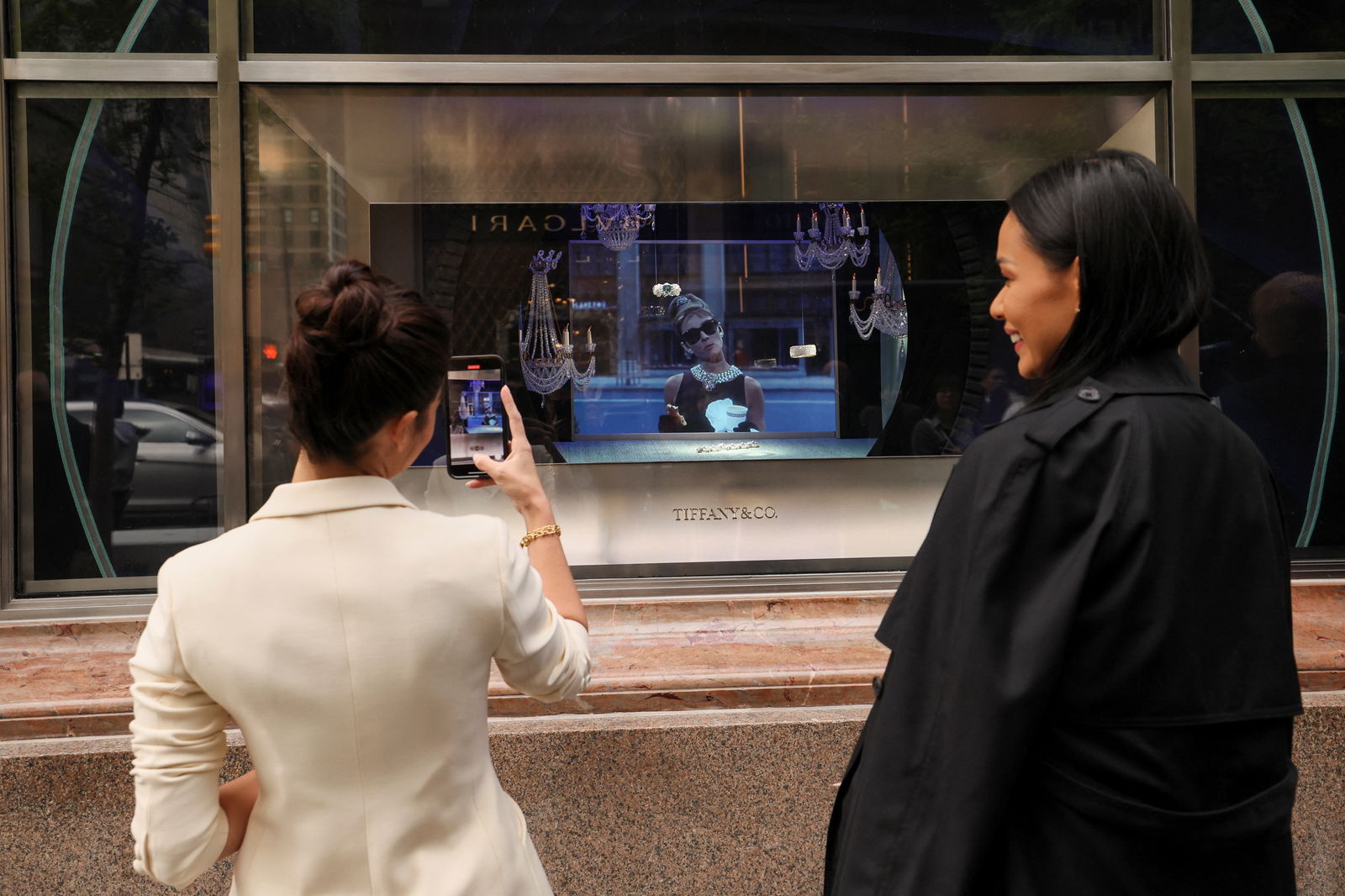 Guests watch as a scene from the movie "Breakfast at Tiffany's" is played in a store window, during a ribbon cutting ceremony for reopening of the Tiffany flagship store on 5th Avenue in Manhattan in New York City, New York, U.S., April 26, 2023. REUTERS/Brendan McDermid