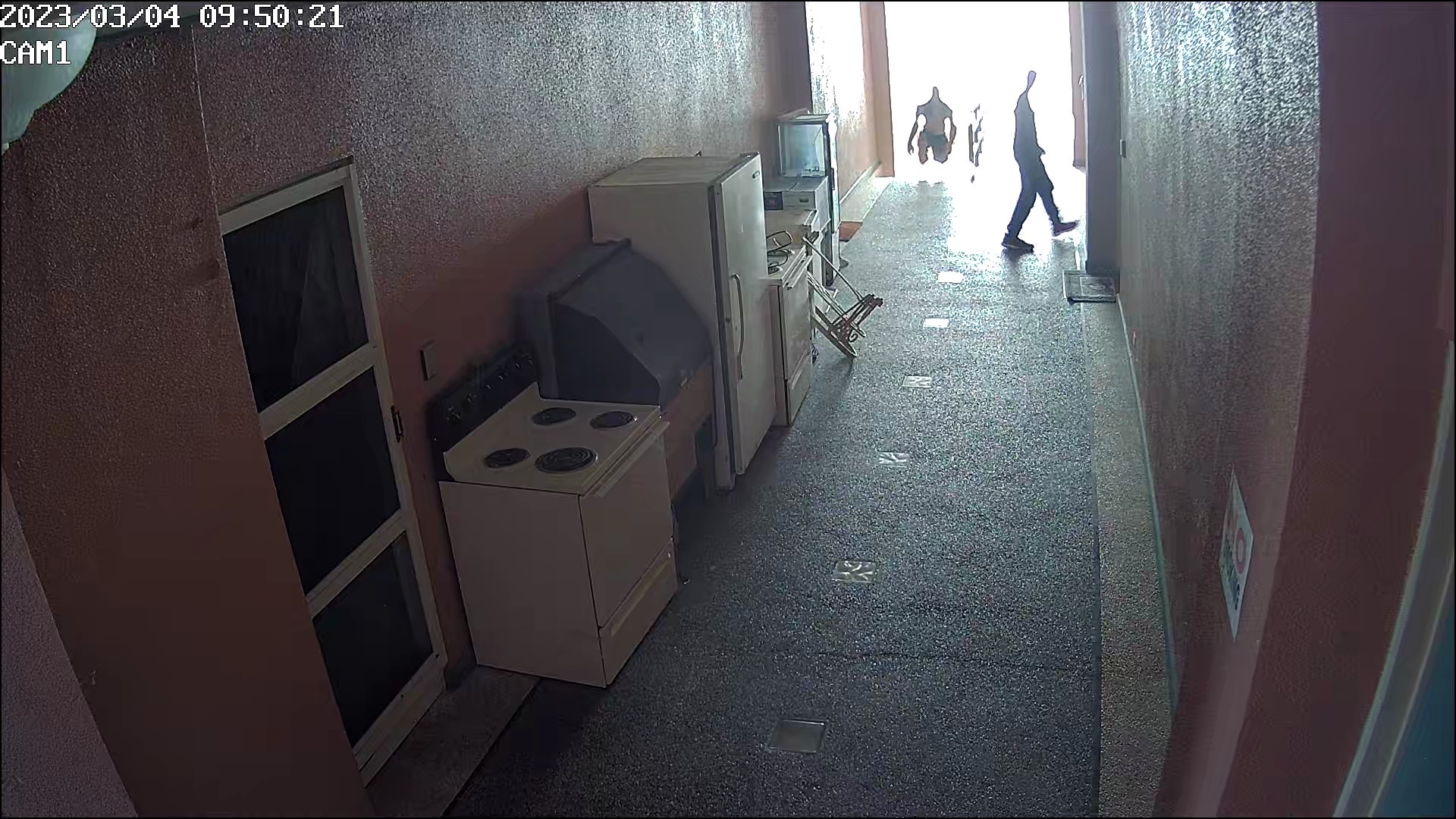 Two individuals are seen entering the third floor walkway of the building where Hideaki Sawada's office is located.