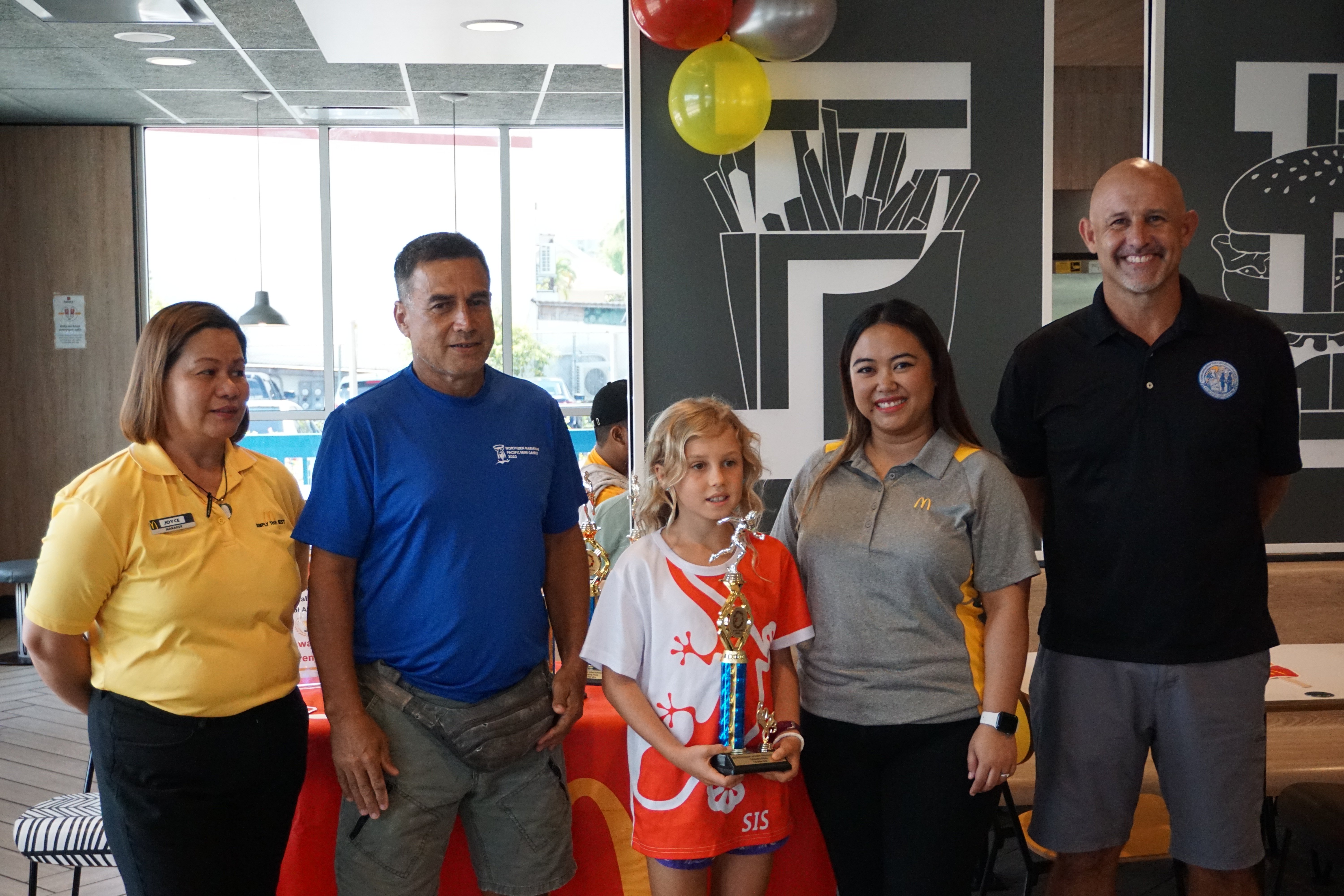 Saipan International School’s Scarlett Burrell, center, the U9 girls MVP, with McDonald's Middle Road general manager Jocelyn Asistores, Northern Marianas Athletics development officer Elias Rangamar, McDonald's of Guam and Saipan Executive Assistant to the President Mable Ayuyu Glenn, and PSS Athletics Program Director Nick Gross, during the awards ceremony at McDonald's Middle Road on Monday.  