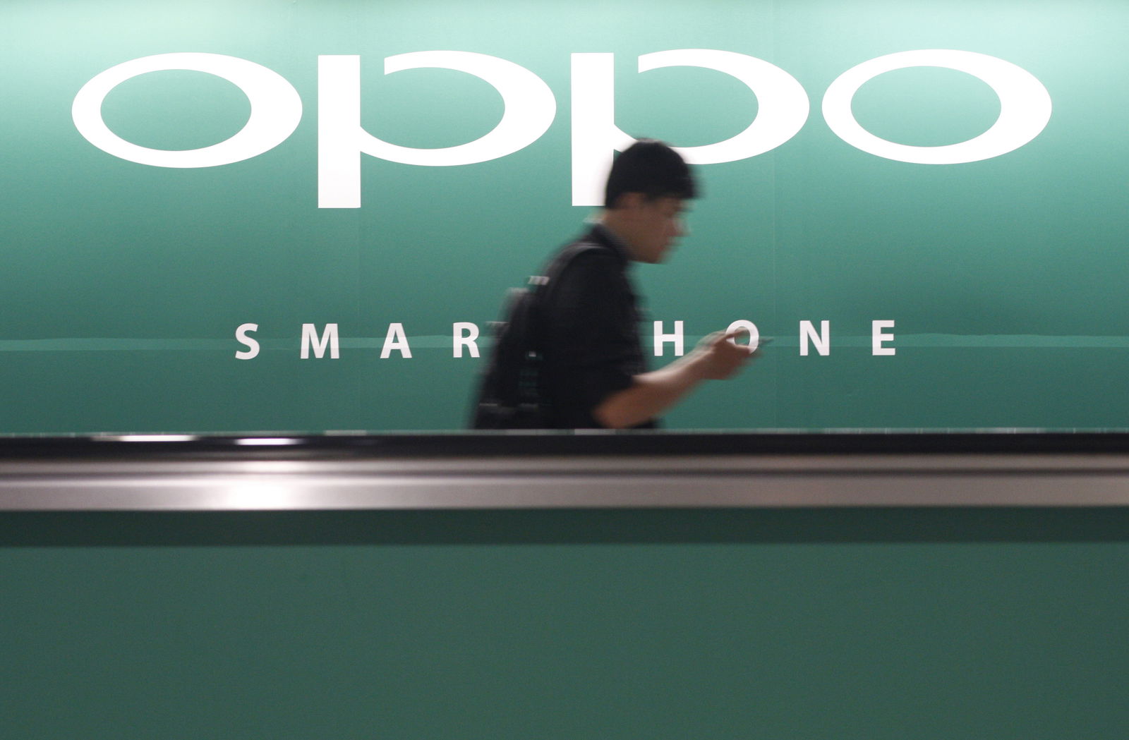 FILE PHOTO: A commuter using his mobile phone passes an advertisement of Chinese smartphone maker Oppo at a train station in Singapore May 8, 2014. REUTERS/Edgar Su