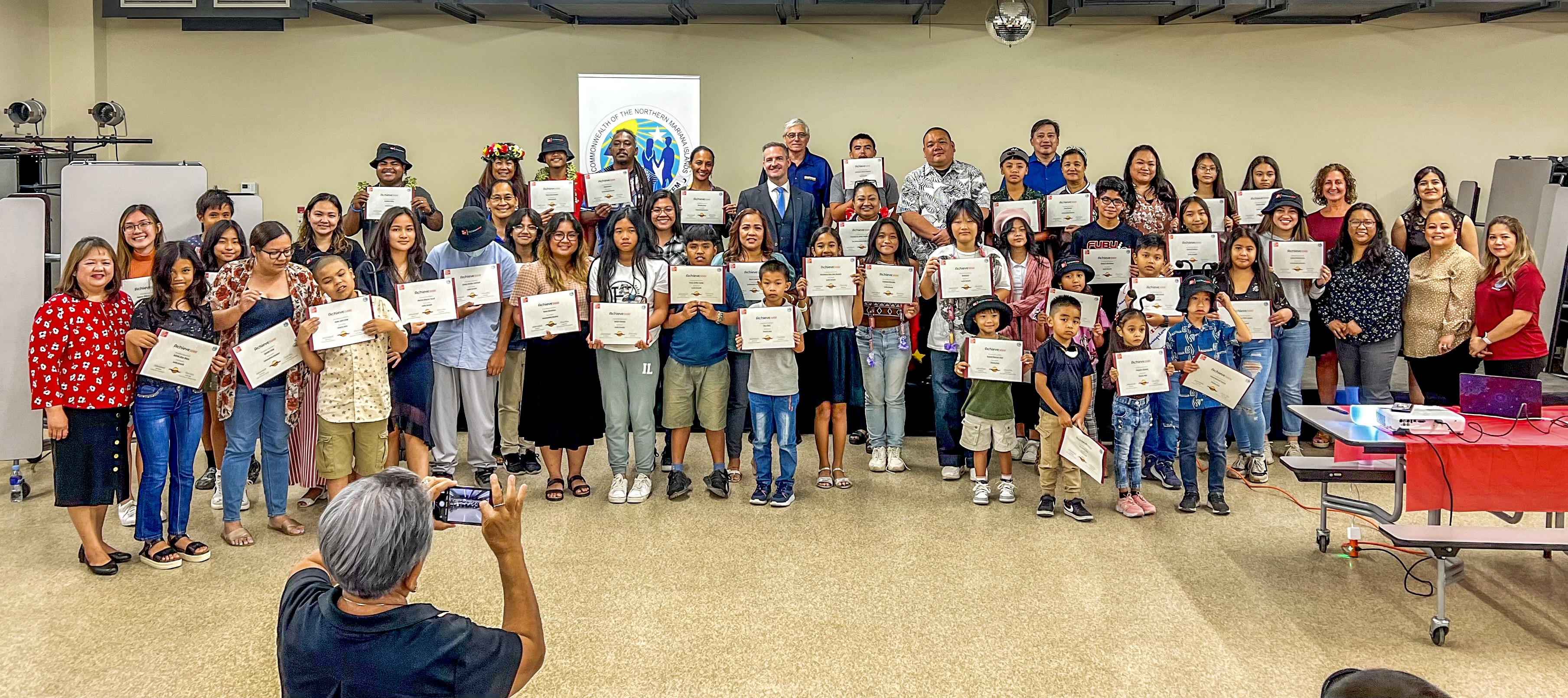Acting Commissioner of Education Eric Magofna, standing background, and Interim Instructional Technology and Distance Education Director Lorraine Catienza pose for a photo with other PSS officials and McGraw Hill/International Achieve3000 Programs’ Patrick Staley and Julie Eckard as they honor students, classroom teachers and schools for their dedication and consistency in using Achieve 3000  on Friday afternoon in the MHS cafeteria. 