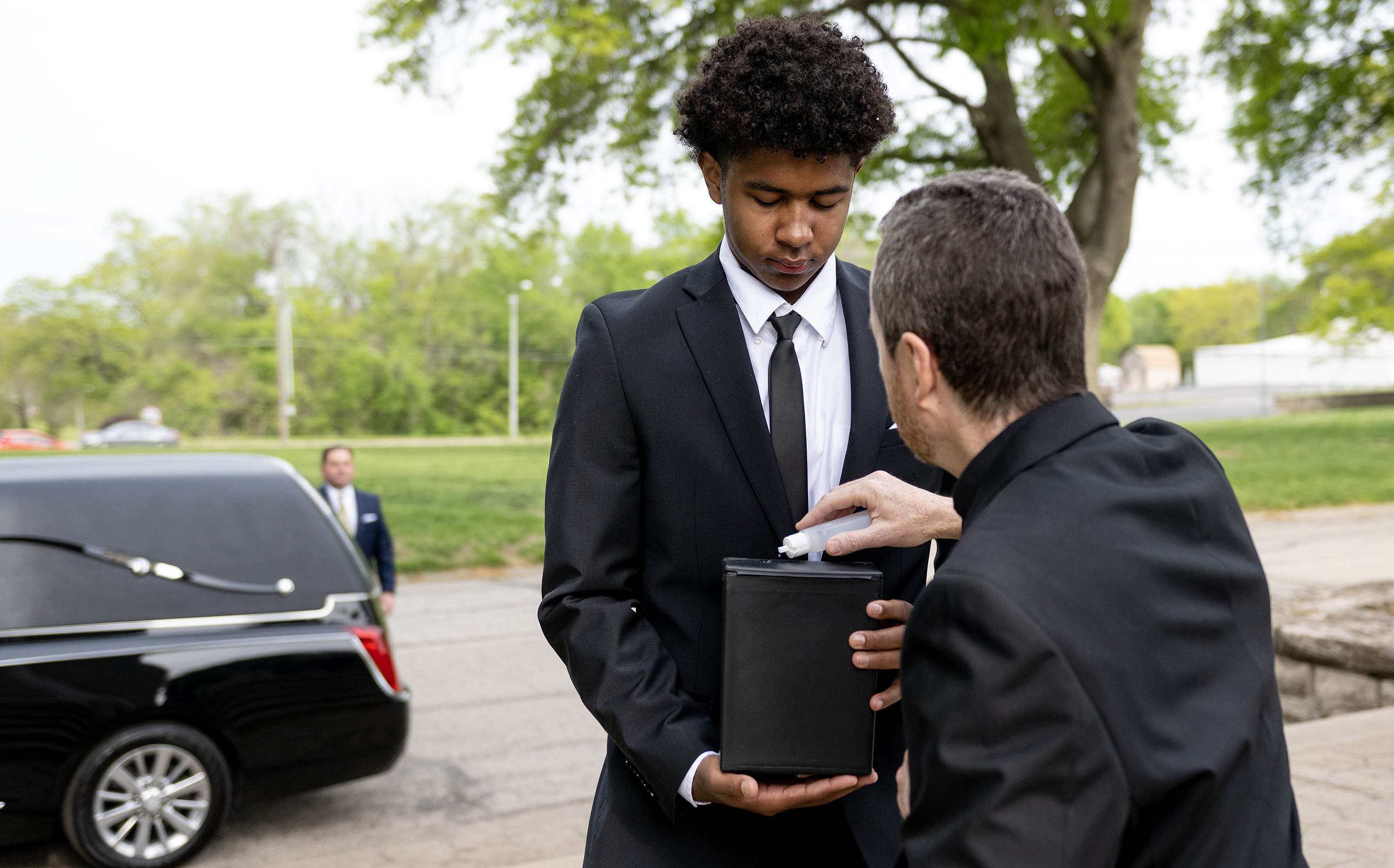 The Rev. Gary Menard blesses a cremated body with holy water as Myles Carson carries it to its final resting place during a funeral service for unclaimed deceased persons at the Mount Olivet Catholic Cemetery on Thursday, May 4, 2023, in Raytown, Missouri. Eight high schoolers from Rockhurst High School helped give the deceased a proper burial service. (Nick Wagner/The Kansas City Star/TNS)