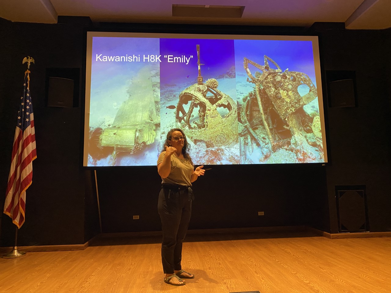 Project lead Jennifer McKinnon stands in front of a picture of “Emily,” a sunken World War II plane that has been the target of artifact theft and graffiti.