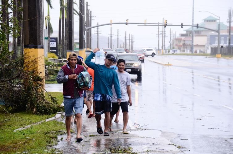 From left: Wilson Castro, Erwin Santos, Erwin Payumo walk along the road in Mongmong-Toto-Maite carrying water and other supplies bought from San Jose Supermarket.