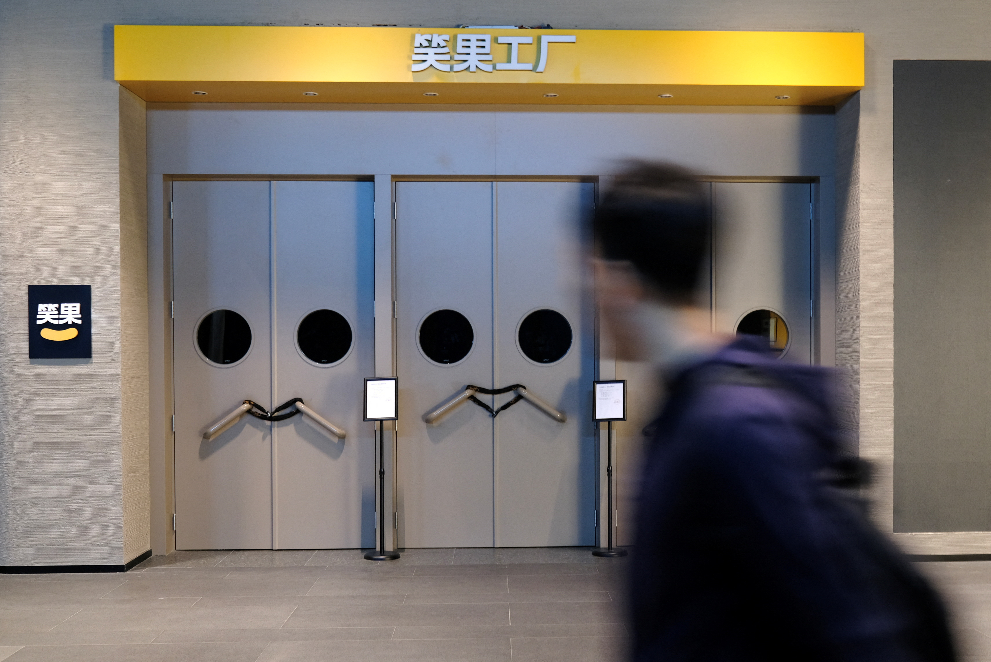 A person walks past a show venue of stand-up comedy company Xiaoguo Culture Media Co that has closed its business with a notice of show cancellation, in Beijing, China May 19, 2023. REUTERS/Tingshu Wang