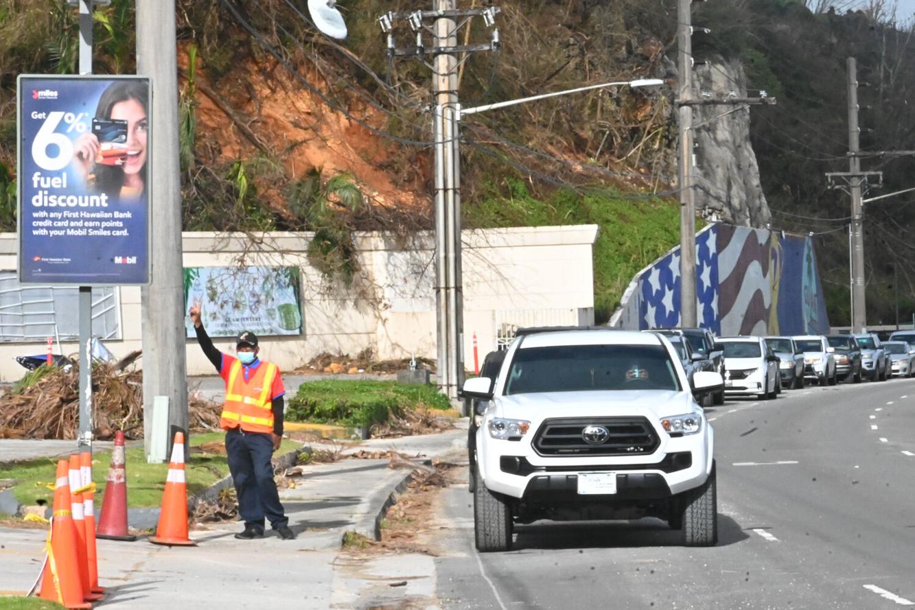 A Mobil gas station employee waves to the camera as he directs cars in a long line to purchase gas Sunday, May 28, 2023, in East Hagåtña.