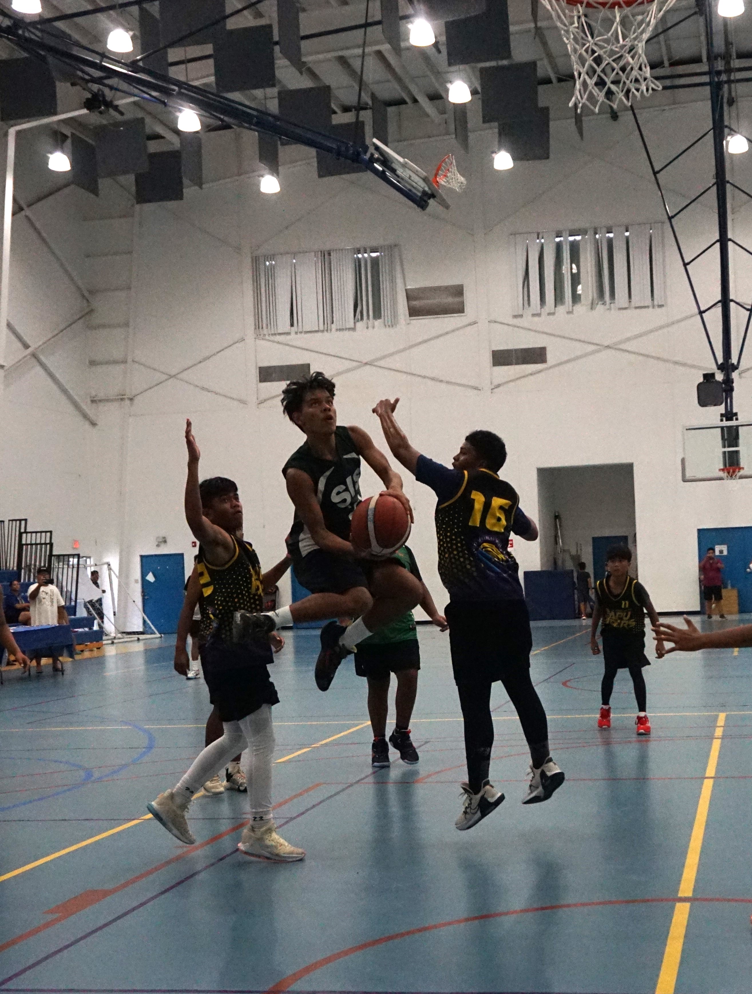 SIS' Aiden Camacho double-clutches between two defenders.