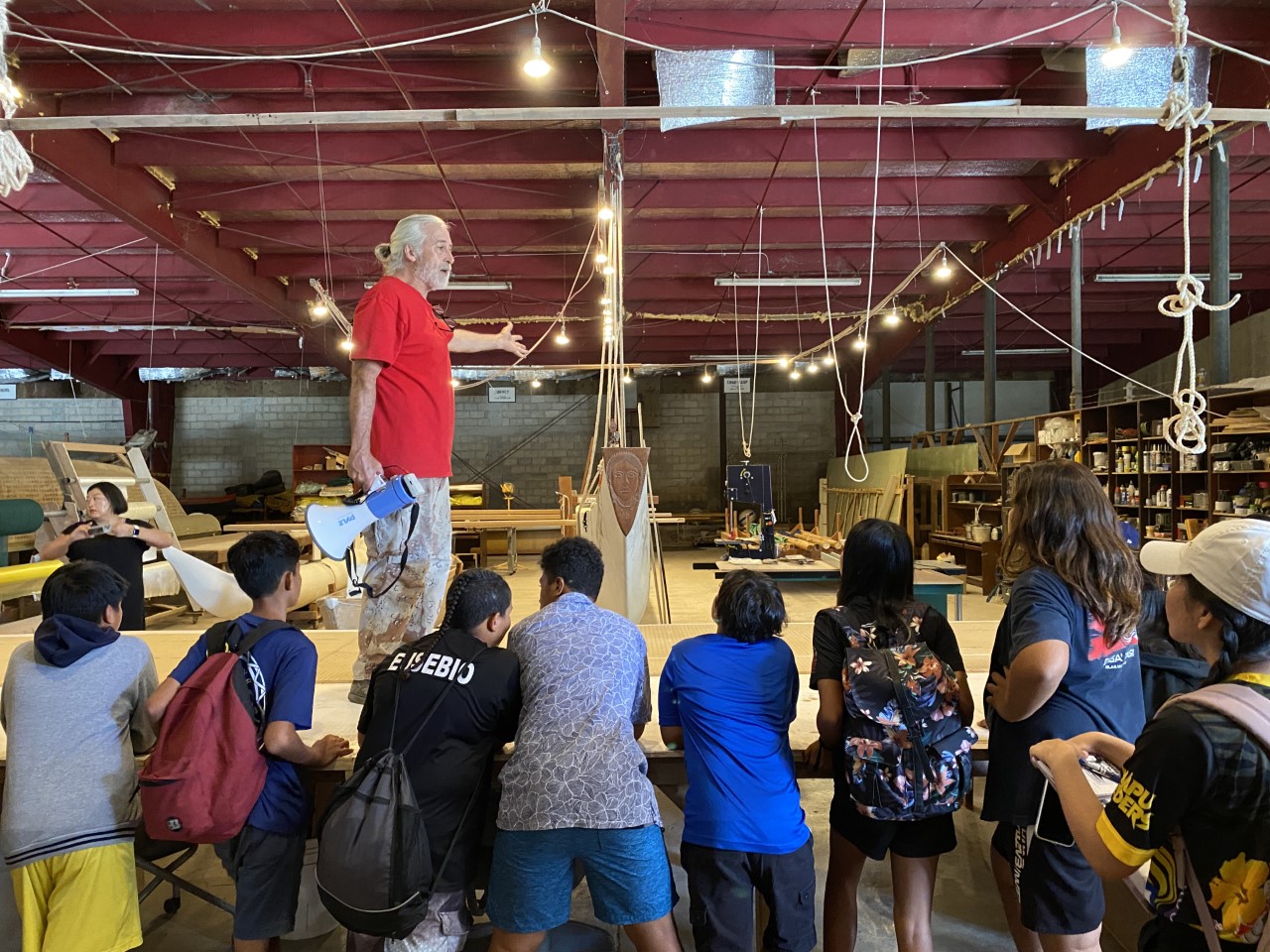 Peter Perez, 500 Sails Executive Director, stands on a table where boat builders infuse fiberglass materials with resin before assembling traditionally designed boats at a later time.