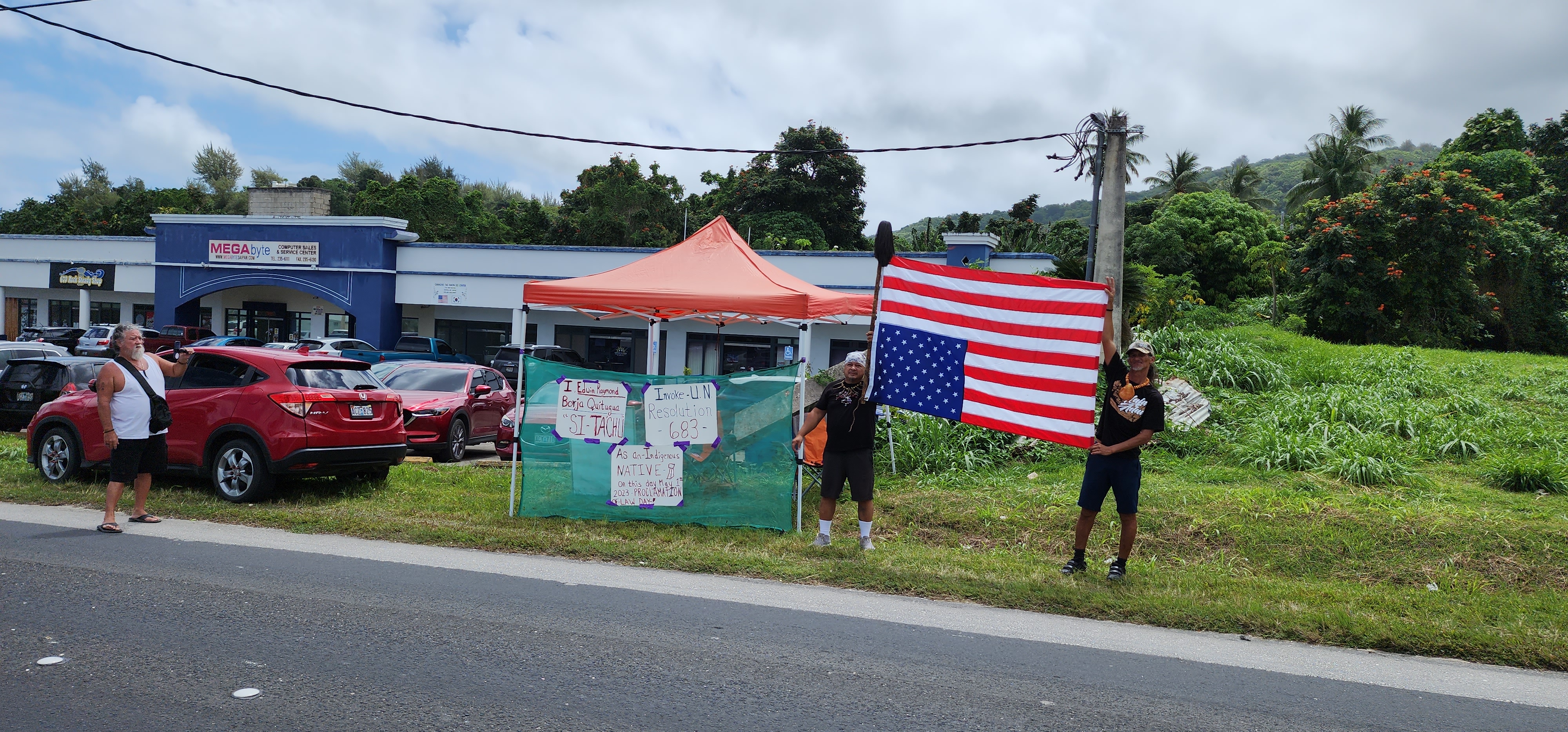 Indigenous Rights advocates Raymond Quitugua and Herman Tudela raise an inverted U.S. flag  during a protest action on Middle Road, across from the United States Courthouse.