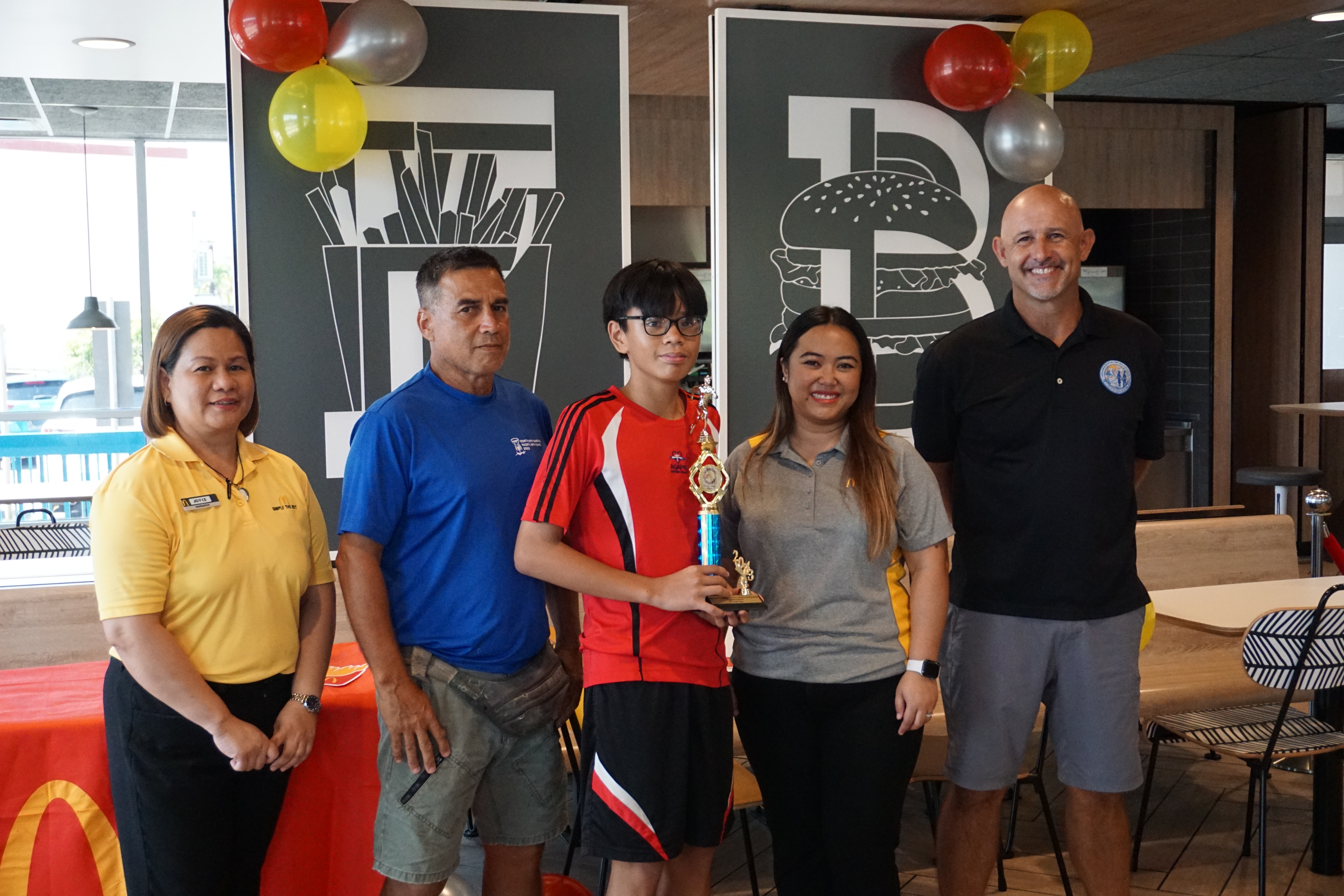 Agape Christian School’s Reyviel Escarlan, center, the U12 boys MVP, with McDonald's Middle Road general manager Jocelyn Asistores, Northern Marianas Athletics development officer Elias Rangamar, McDonald's of Guam and Saipan Executive Assistant to the President Mable Ayuyu Glenn, and PSS Athletics Program Director Nick Gross, during the awards ceremony at McDonald's Middle Road on Monday.  