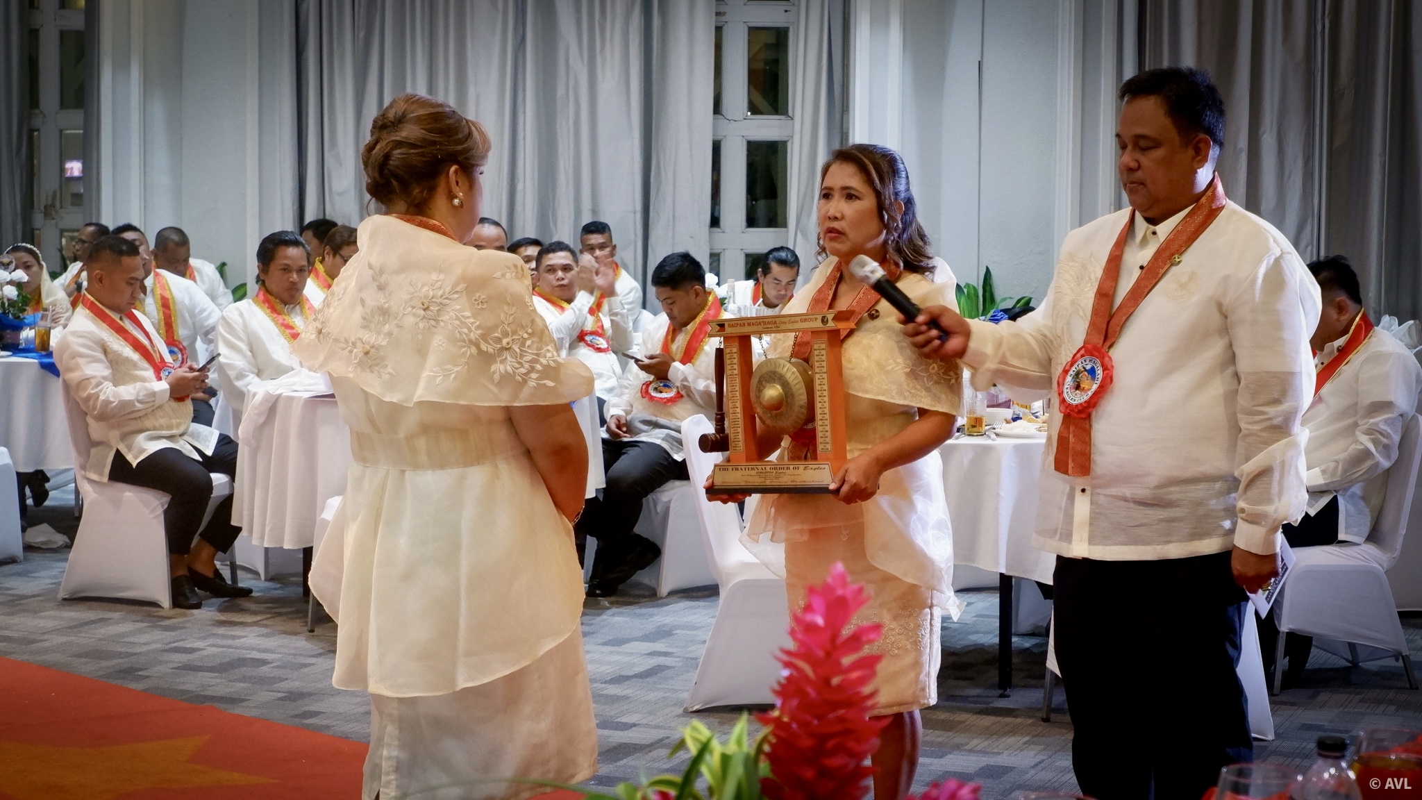 Assisted by Saipan Maga'lahi Eagles Club Past President Eagle Marlon Regaton, right, Saipan Maga'Haga Lady Eagles Group’s Past President Lady Eagle Angelica Lastimado, left, turns over the gong and gavel to her successor, Lady Eagle Yolanda De Ramos.