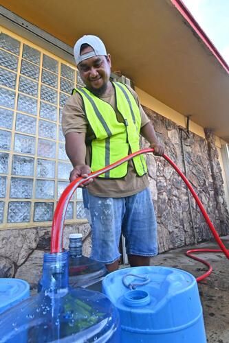 Mayor's office staff member Jason Timothy uses a hose to fill residents' water bottles Sunday in Mangilao.