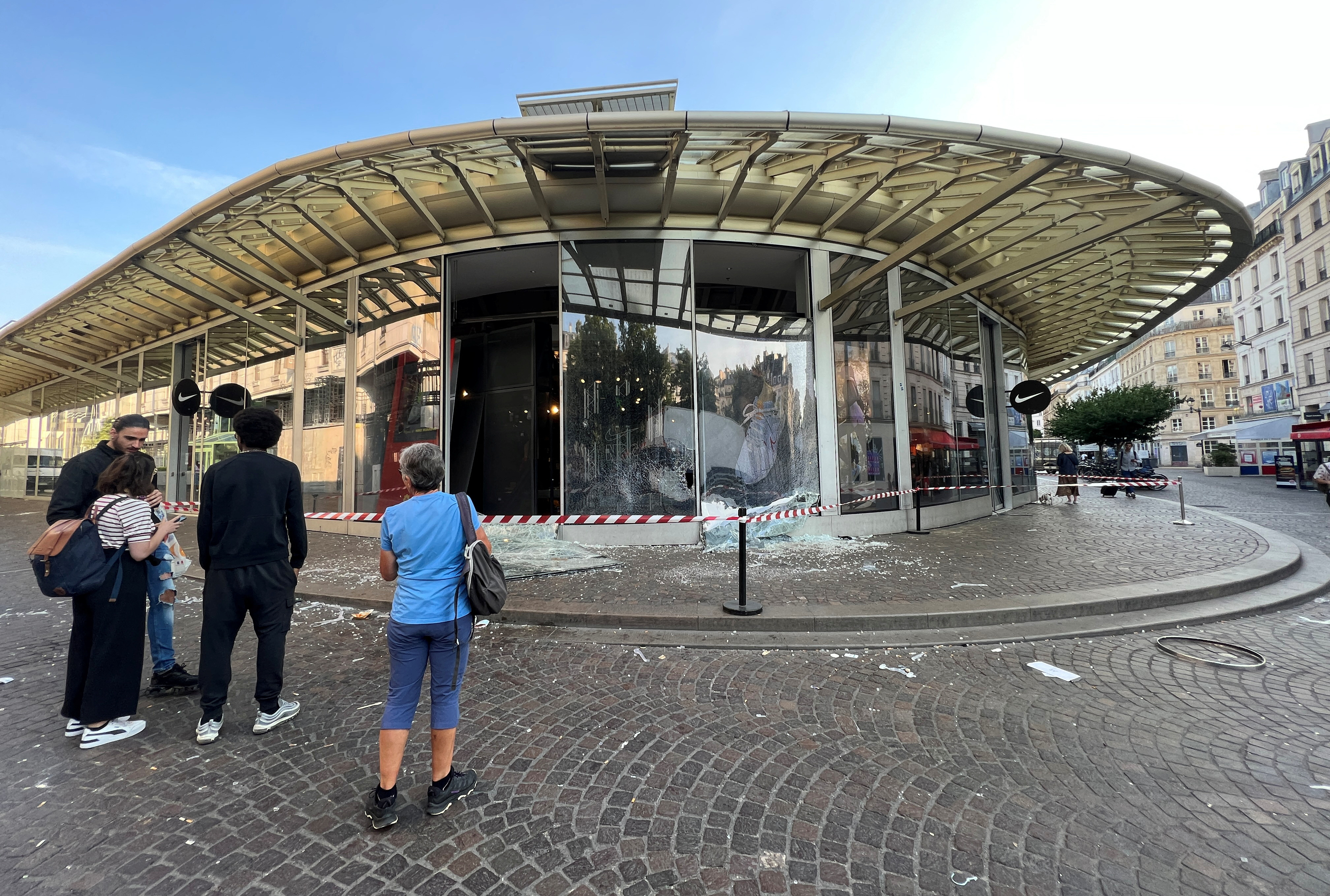 People stand in front of a Nike store vandalised during a night of clashes between protesters and police following the death of Nahel, a 17-year-old teenager killed by a French police officer in Nanterre during a traffic stop, at the Westfield Forum des Halles shopping centre in Paris, France, June 30, 2023. REUTERS/Lucien Libert
