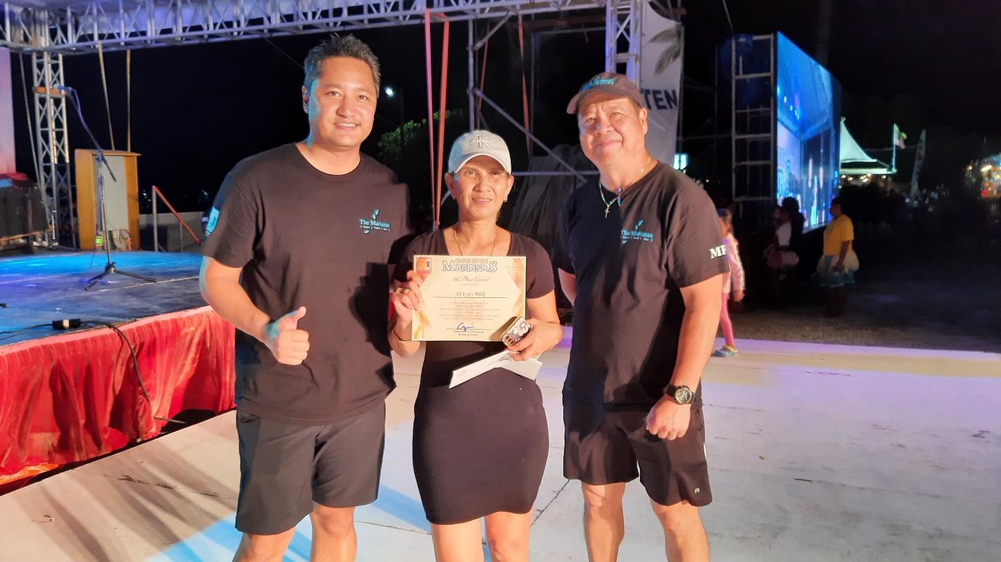 Marianas Visitors Authority Managing Director Christopher A. Concepcion, left, presents the 4th place award to Rizalyn Joson of Vi-lyn’s BBQ on June 24, 2023, in the booth decorating contest at the 24th Annual Taste of the Marianas International Food Festival & Beer Garden, at Garapan Fishing Base in Saipan.  At right is MVA Community Projects Manager Martin Duenas. 