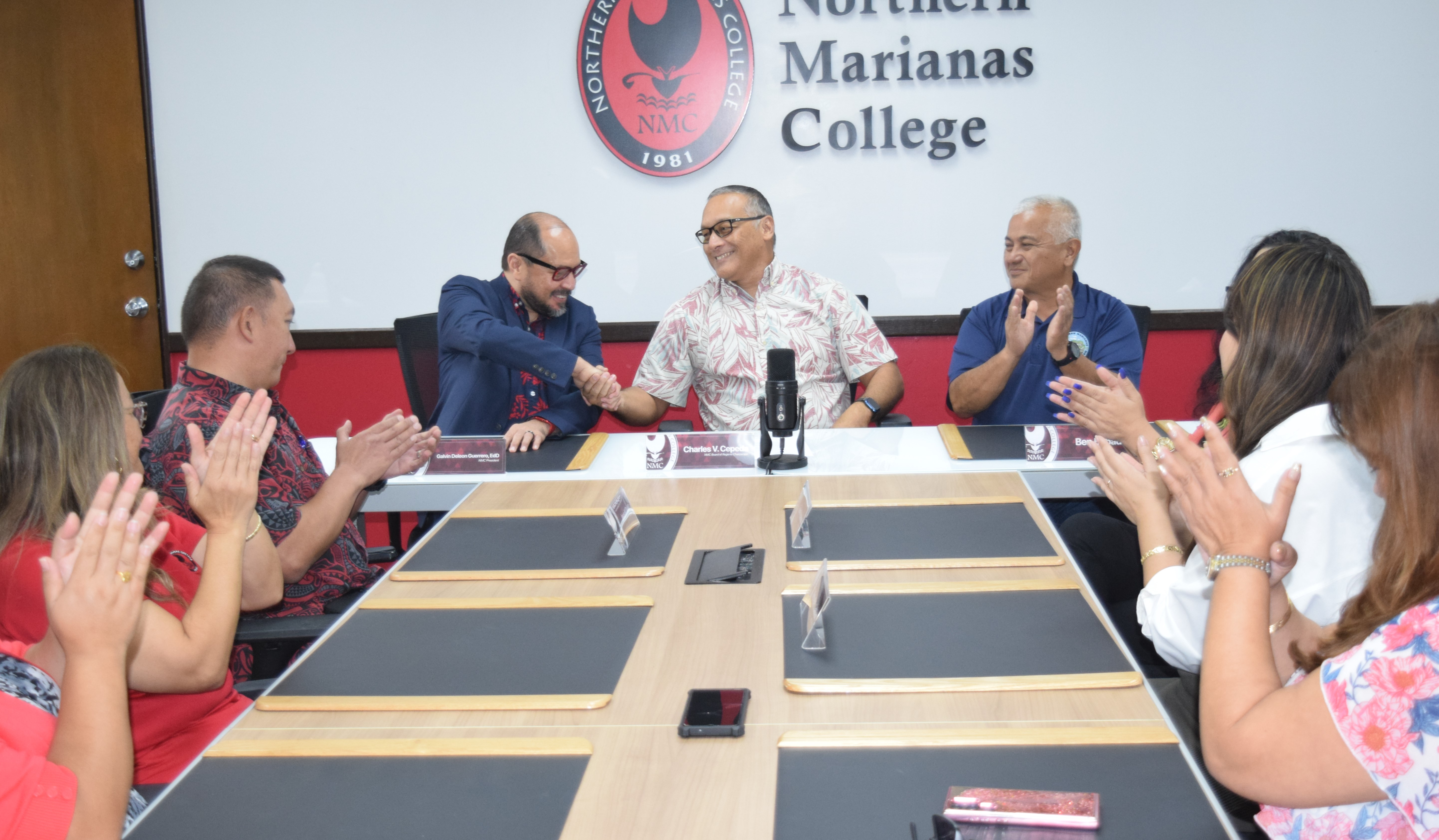 Northern Marianas College President Dr. Galvin S. Deleon Guerrero, left, shakes hands with NMC Board of Regents Chairman Charles V. Cepeda, center, as NMC Foundation Chairman Vicente Babauta, third right, and other members of the Board of Regents applaud in the NMC Board of Regents conference room on Thursday.