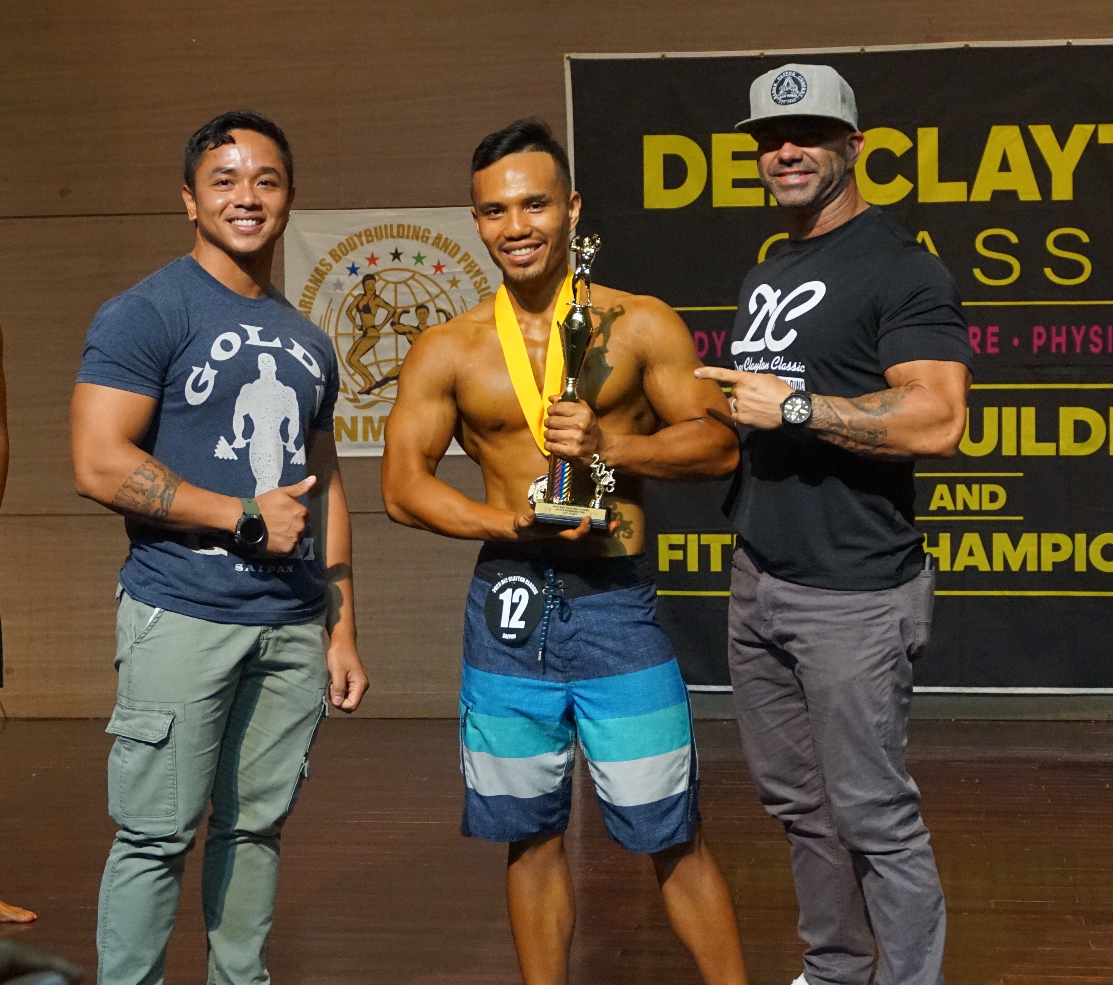 Enrico Valdez, center, holds the men's physique overall trophy as he poses for a photo with Gold’s Gym certified personal trainer Gerald Galang, left, and Latte Built owner Derek Cutting, right, at the conclusion of the 2023 Dee Clayton Classic & Northern Marianas Bodybuilding Federation competition at Saipan World Resort's Taga Hall.