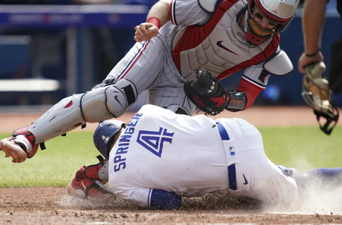 Toronto Blue Jays' George Springer (4) dives for home plate and collides with Minnesota Twins catcher Ryan Jeffers (27) during the fifth inning of a baseball game in Toronto, Saturday, June 10, 2023. Springer was safe on the play.