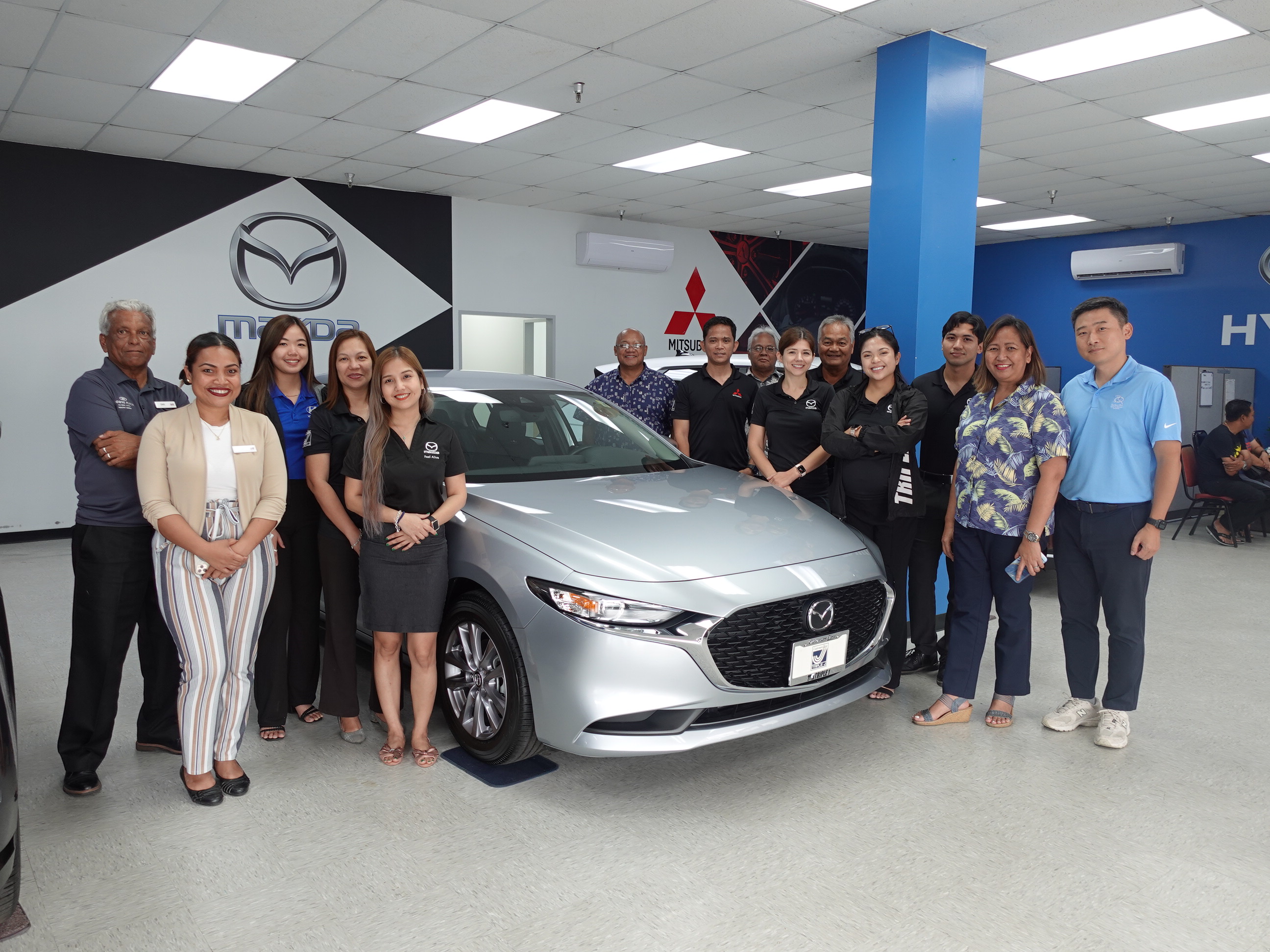 Triple J Motors Sales Manager Steve Sablan, seventh right, presents a 2023 Mazda 3 Hatchback Sport Sedan in their showroom for the 21st Annual HANMI Charity Classic Golf Tournament, scheduled for July 15, 2023, at LaoLao Bay Golf & Resort west course in Saipan.   Also pictured are other Triple J Motors management and staff and members of the HANMI Charity Classic Golf Tournament Committee.