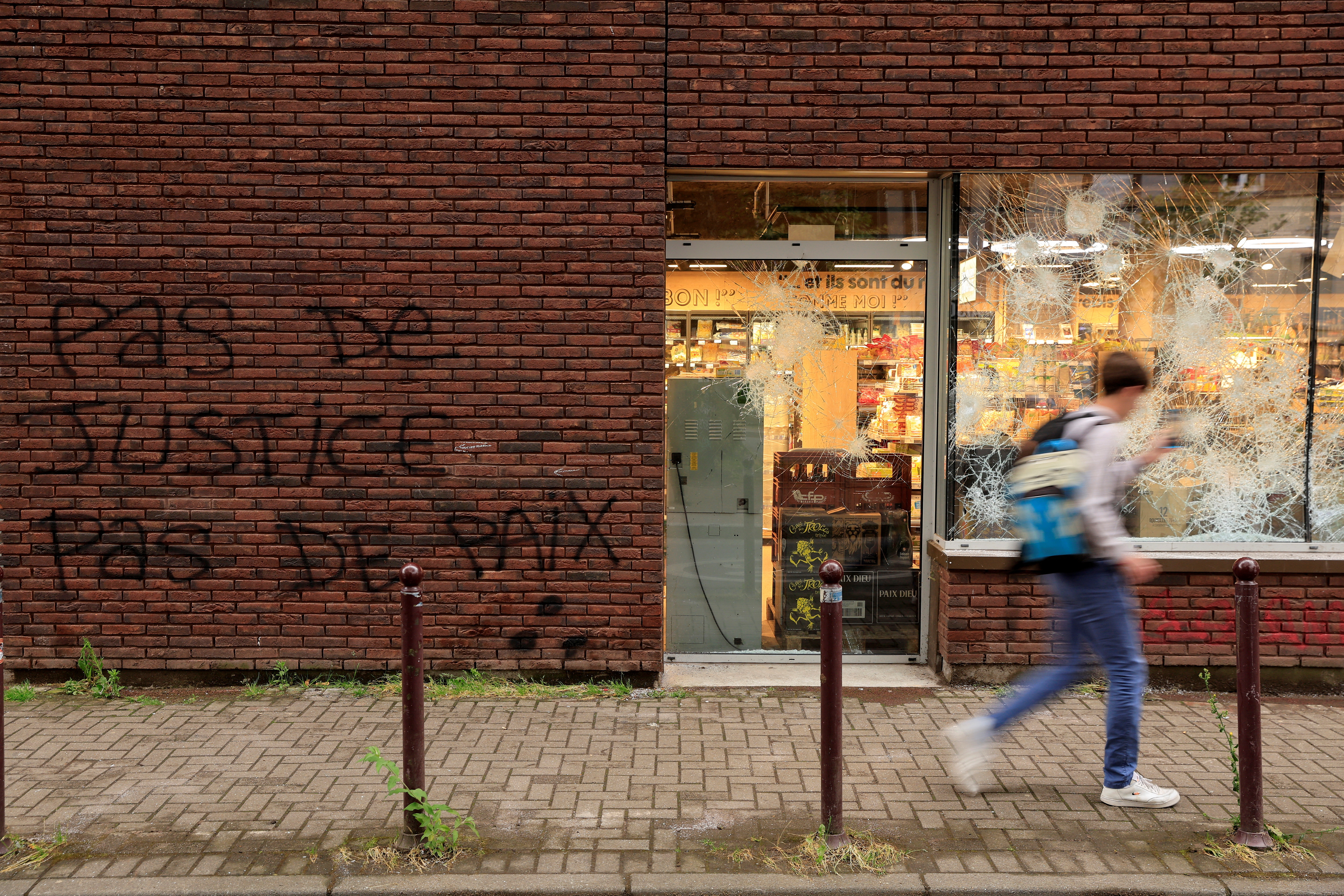 A man walks past a shop vandalised during night clashes between protesters and police, following the death of Nahel, a 17-year-old teenager killed by a French police officer in Nanterre during a traffic stop, in Lille, northern France, June 30, 2023. The slogan on the wall reads "No justice, no peace". REUTERS/Pascal Rossignol