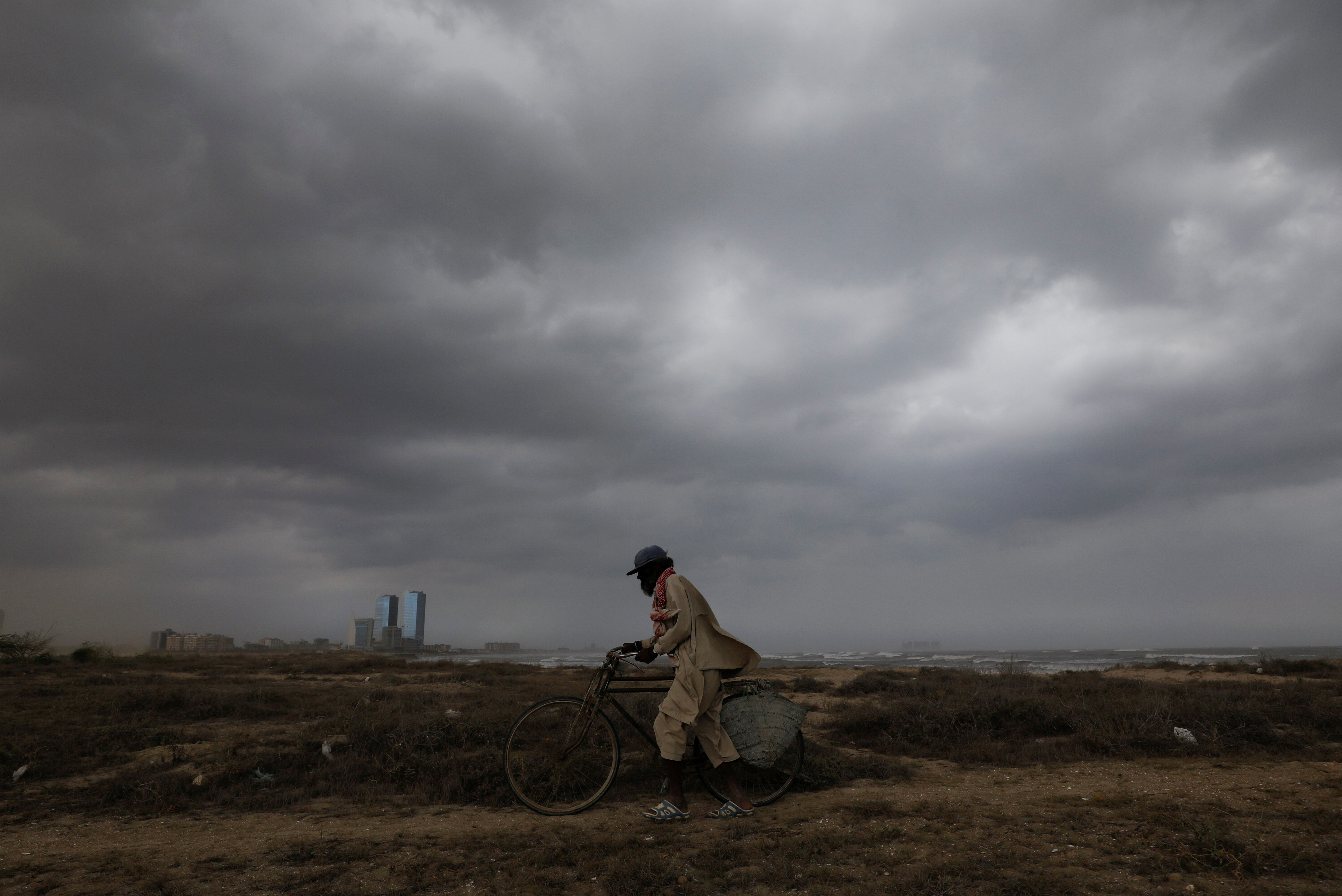 Abdullah, 50, a fisherman, walks with his bicycle with rain clouds in the background, before the arrival of cyclonic storm, Biparjoy, over the Arabian Sea, in Karachi, Pakistan June 15, 2023. REUTERS/Akhtar Soomro