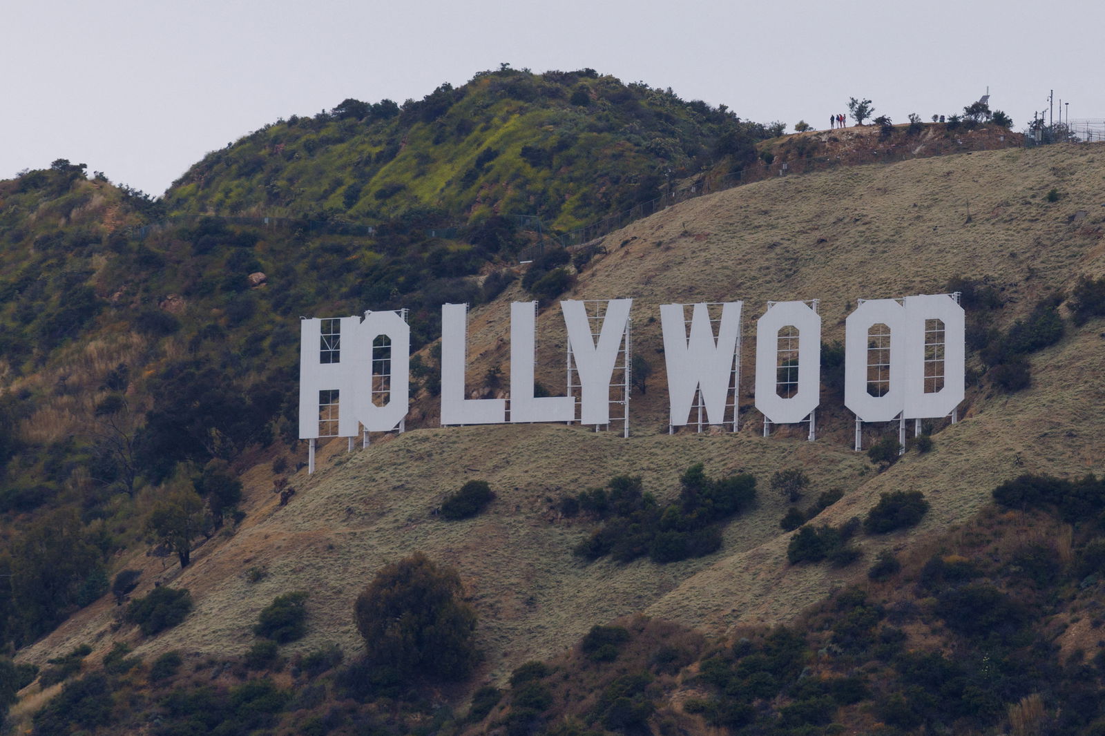 FILE PHOTO: People stand above the Hollywood sign under a cloudy sky in Los Angeles, California, U.S., May 31, 2023. REUTERS/Mike Blake/File Photo